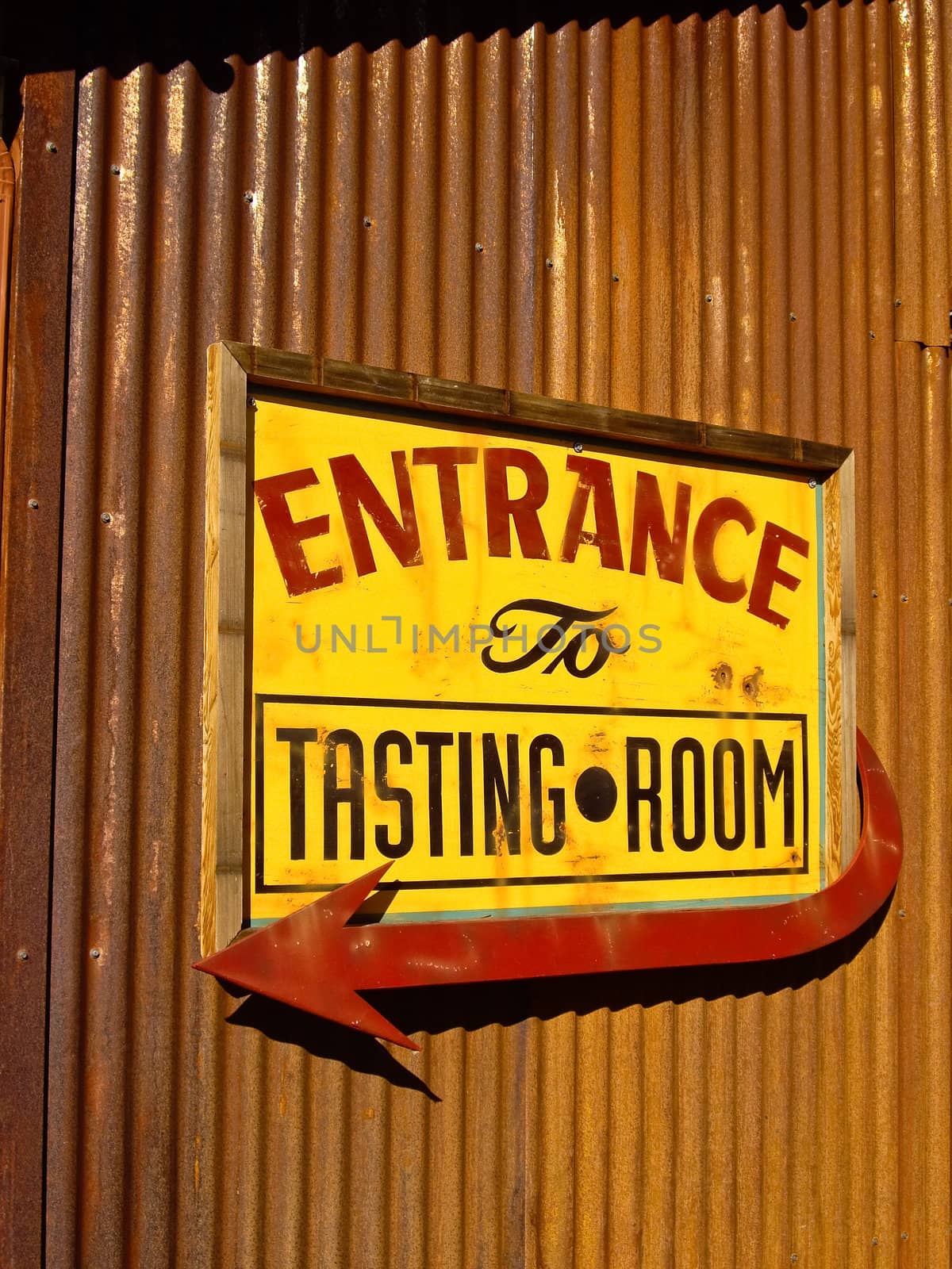 Red and yellow wine tasting entrance sign on rusted metal wall