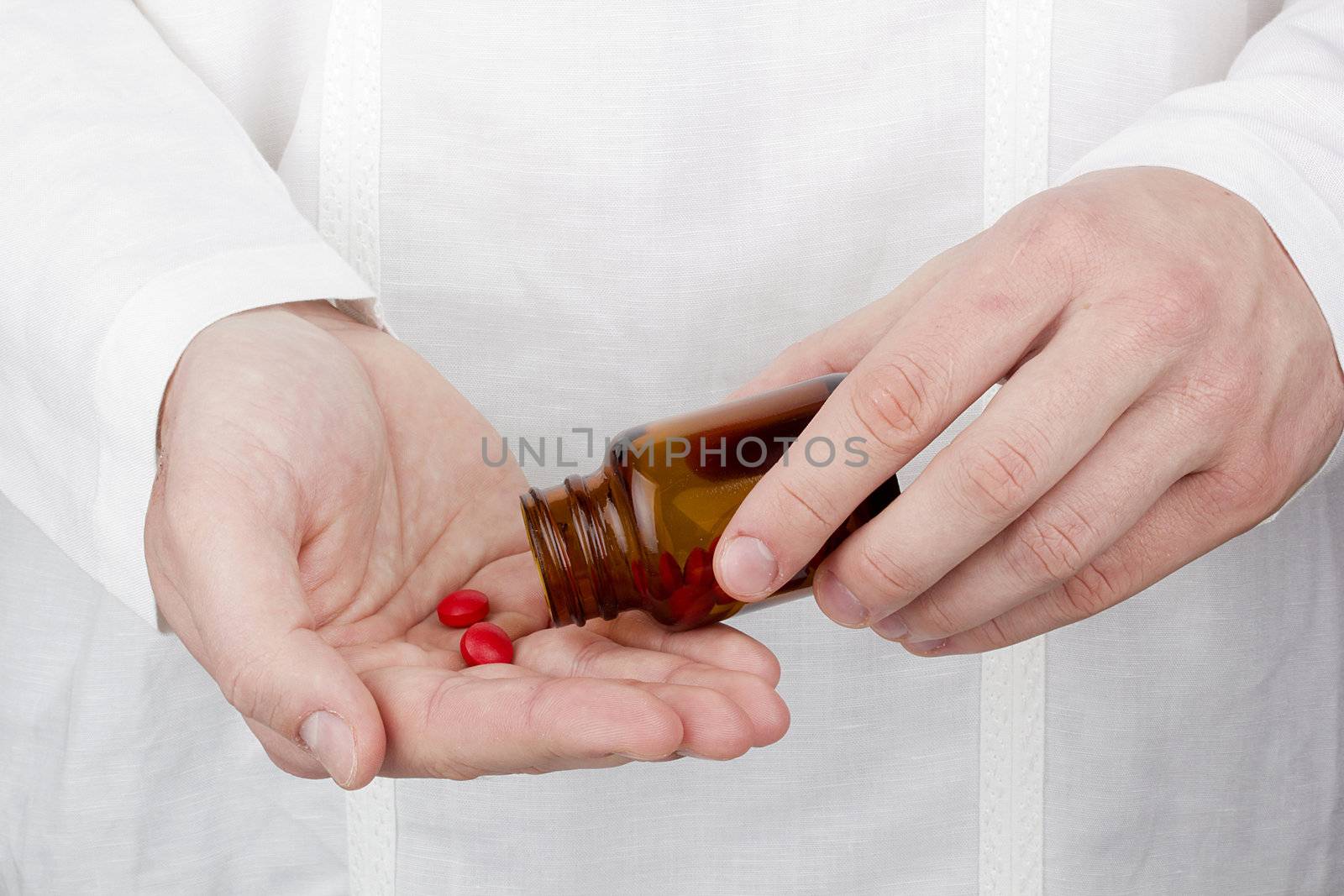 Close-up photograph of a hand pouring red tablets out of a transparent bottle into another hand.