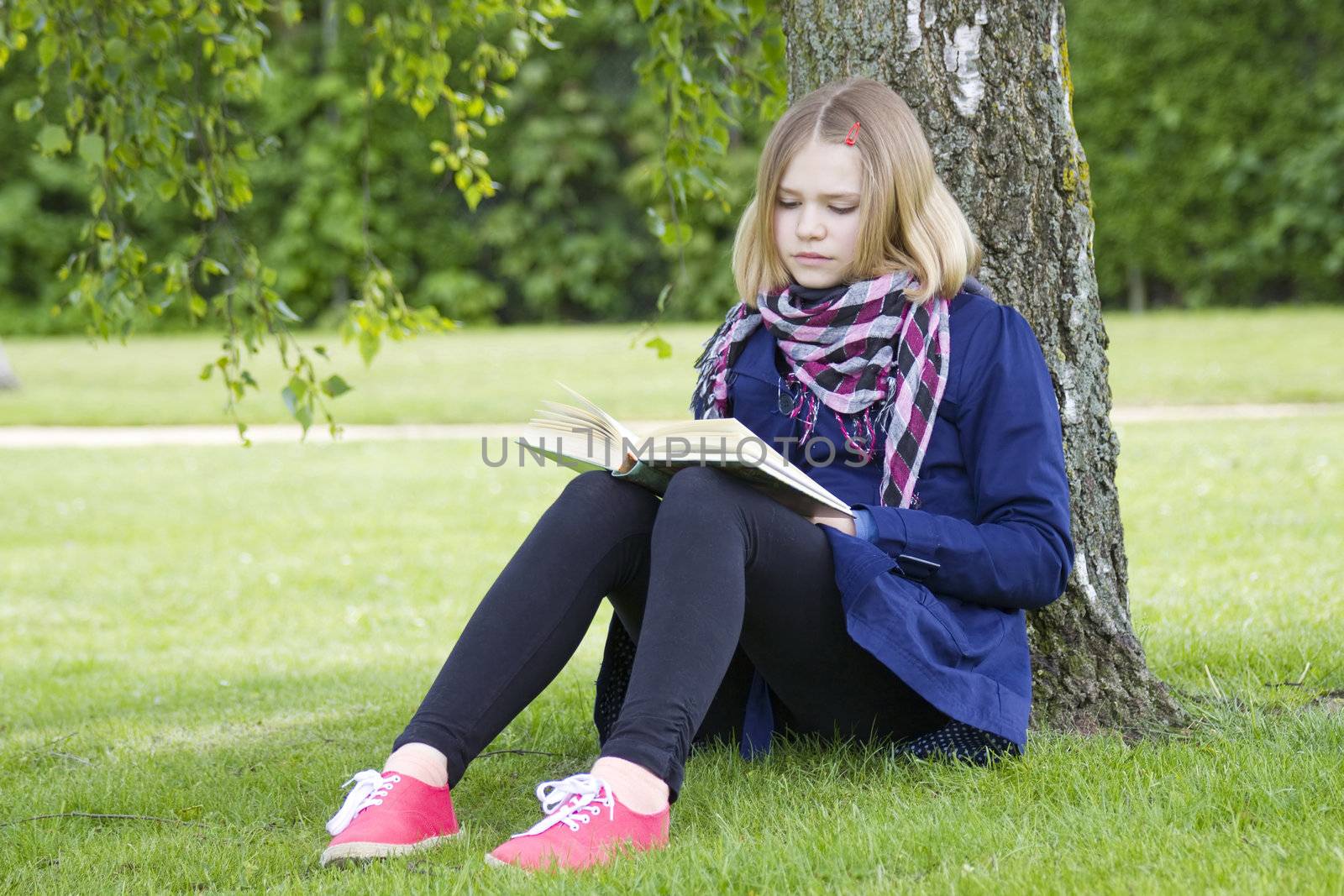 Young girl reading book in park in spring day  by miradrozdowski