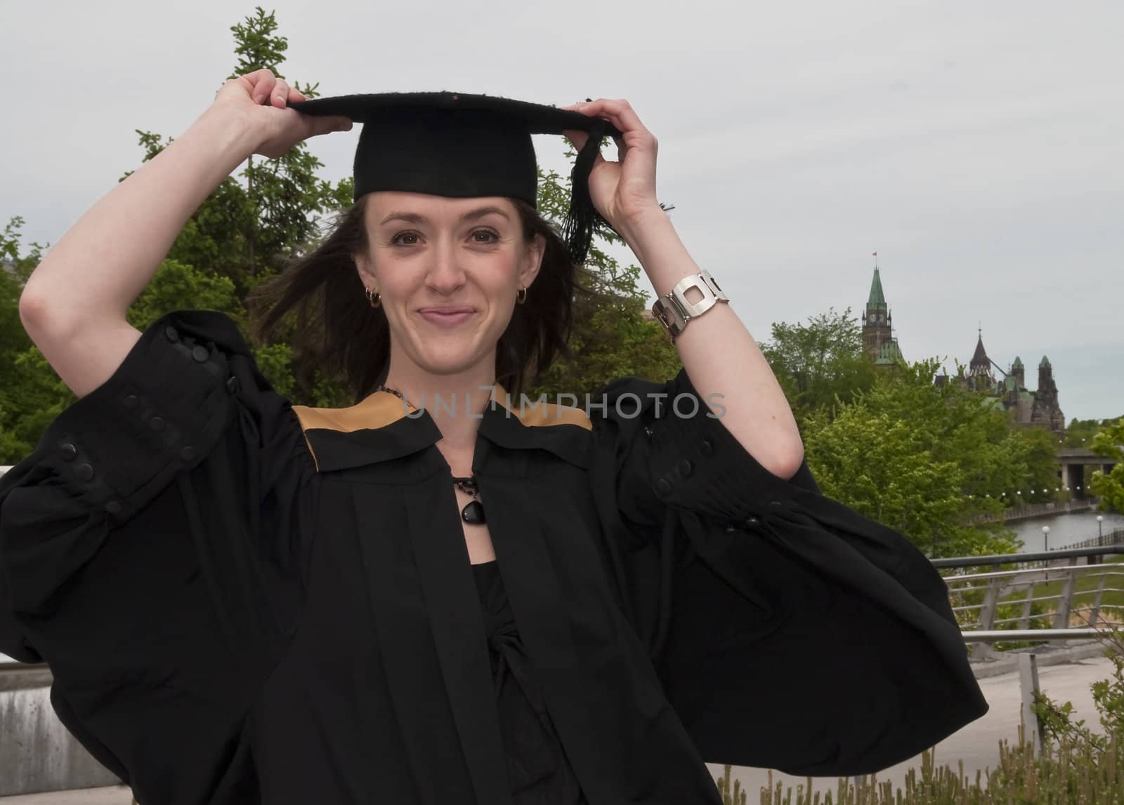 Young woman holding graduation hat on windy day.