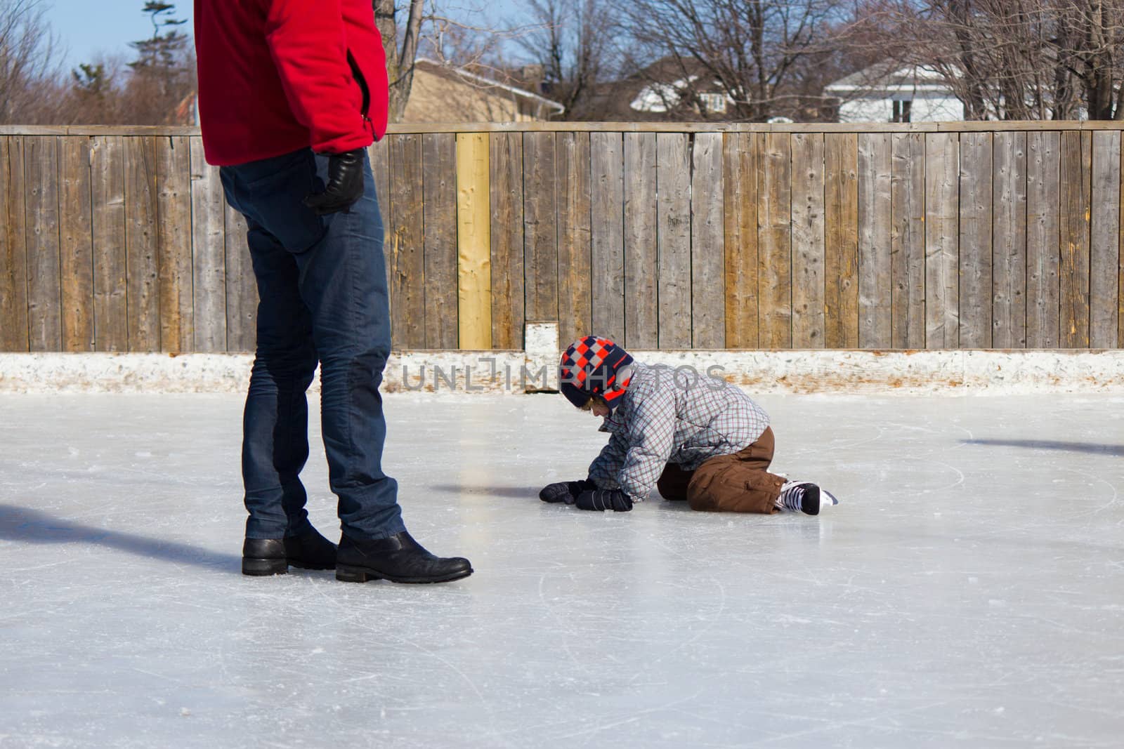 Father teaching son how to ice skate at an outdoor skating rink in winter.