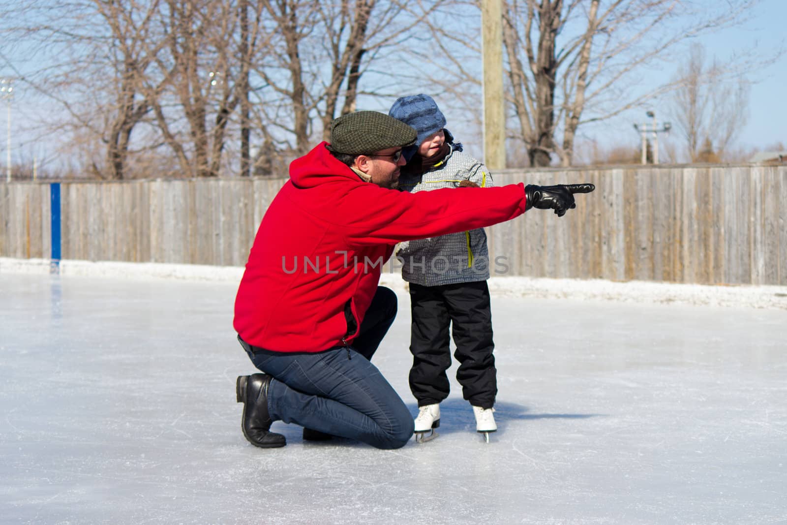 Father teaching daughter how to ice skate at an outdoor skating rink in winter.