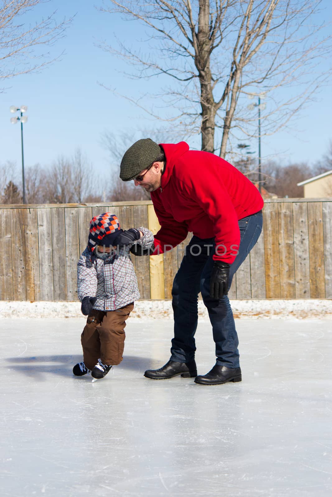 Father teaching son how to ice skate at an outdoor skating rink in winter.