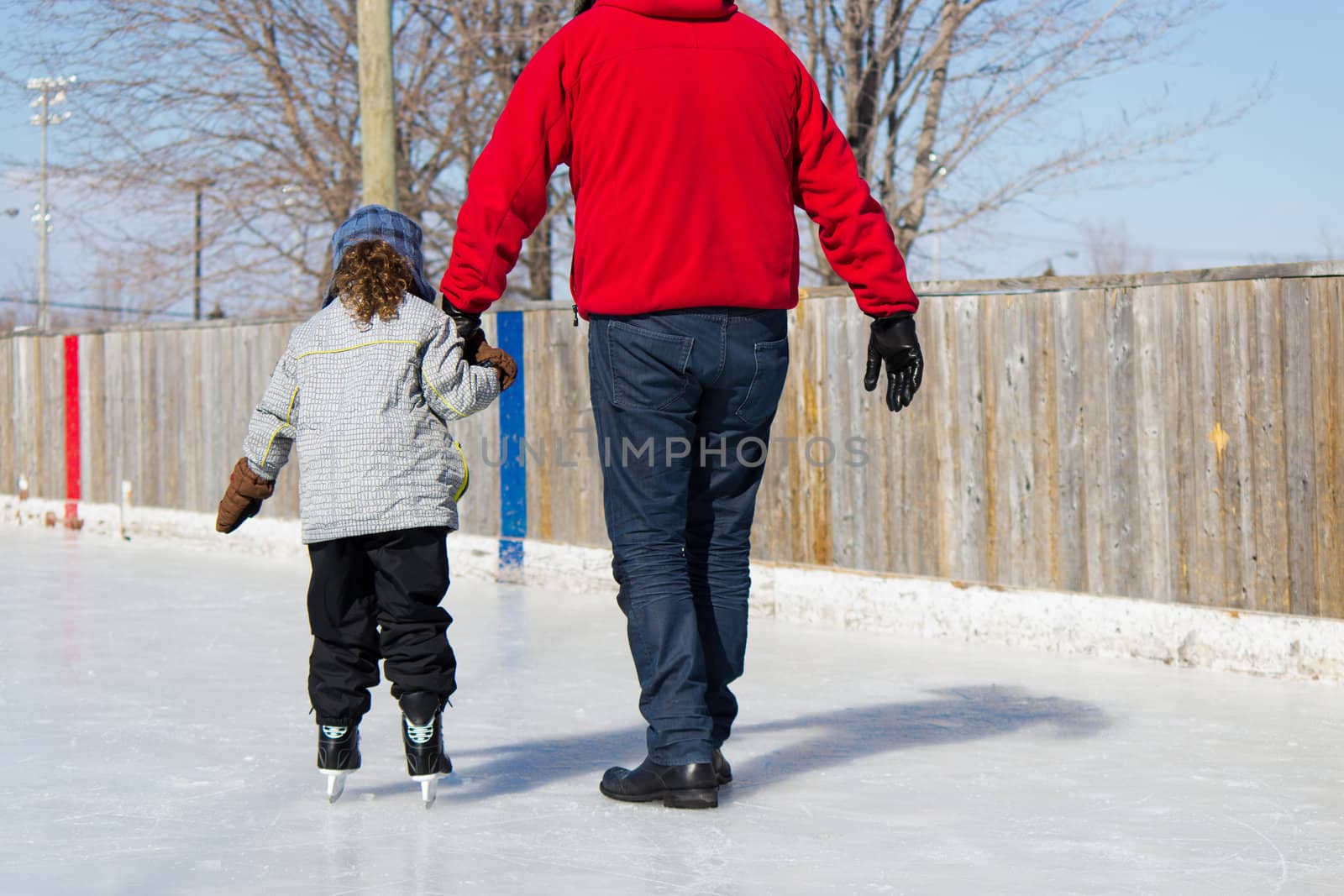 Father teaching daughter how to ice skate at an outdoor skating rink in winter.