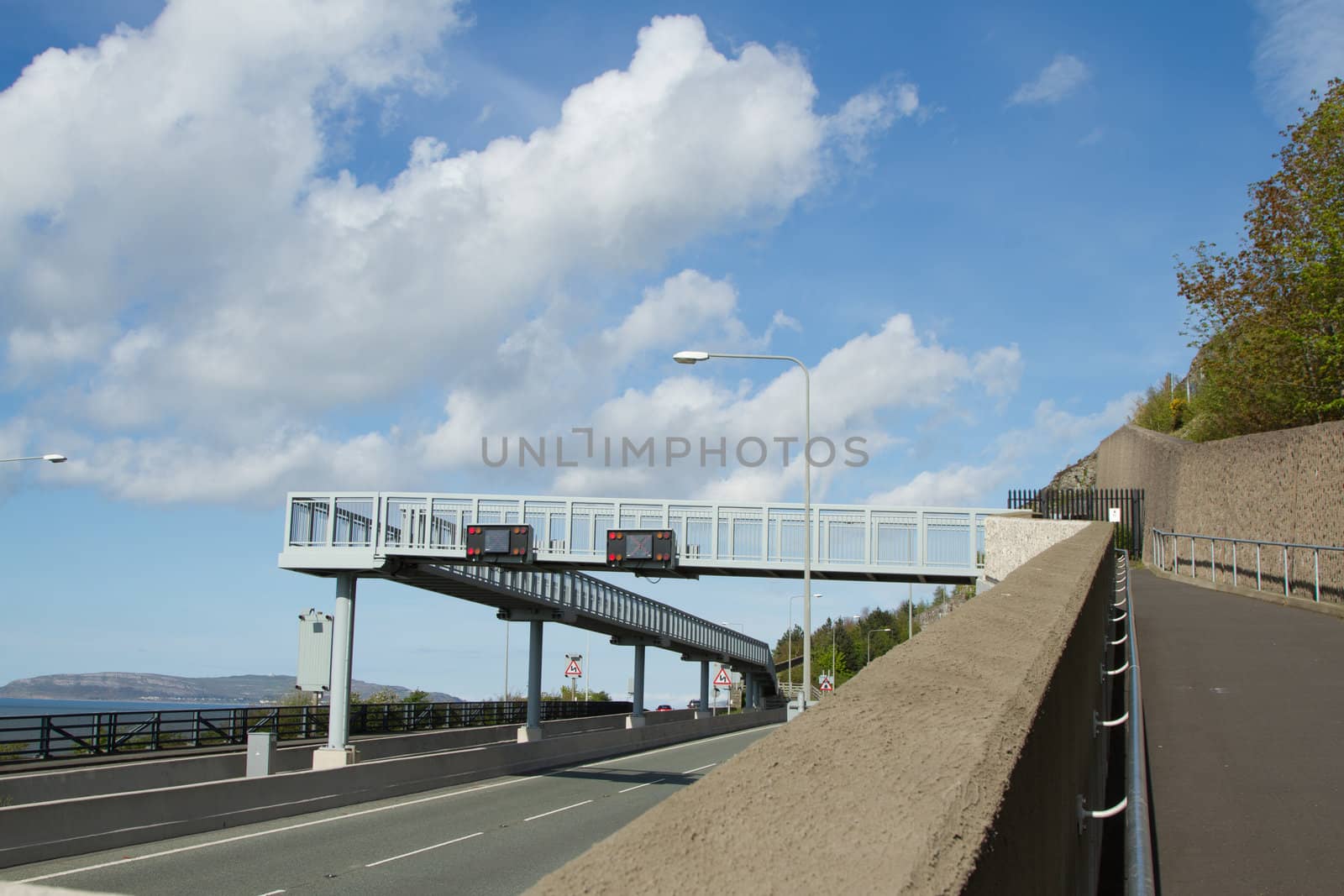 A pair of electronic traffic signs fixed to a raised metal walkway with a cloudy sky in the background.