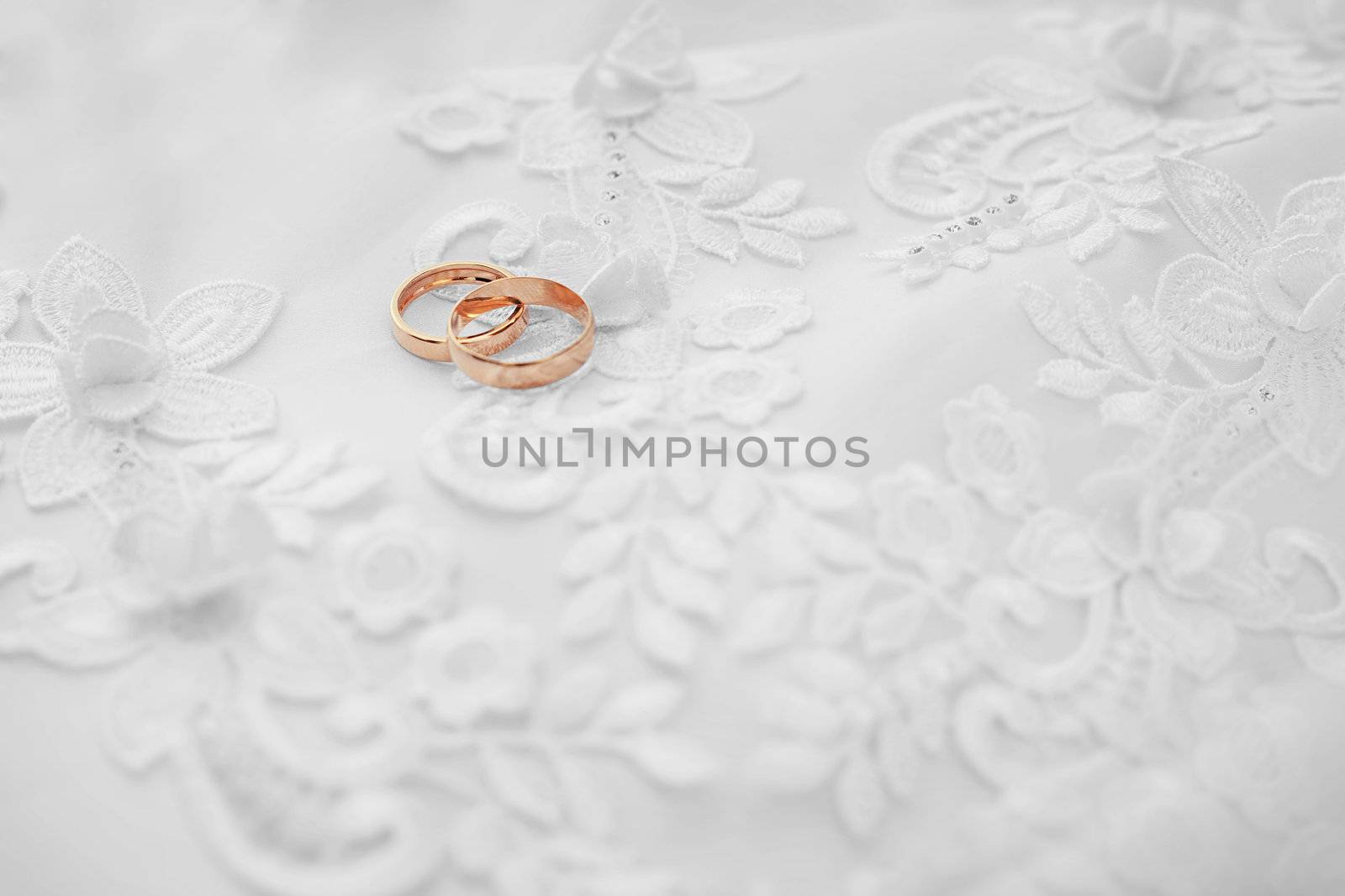 Two gold wedding rings on white dress background