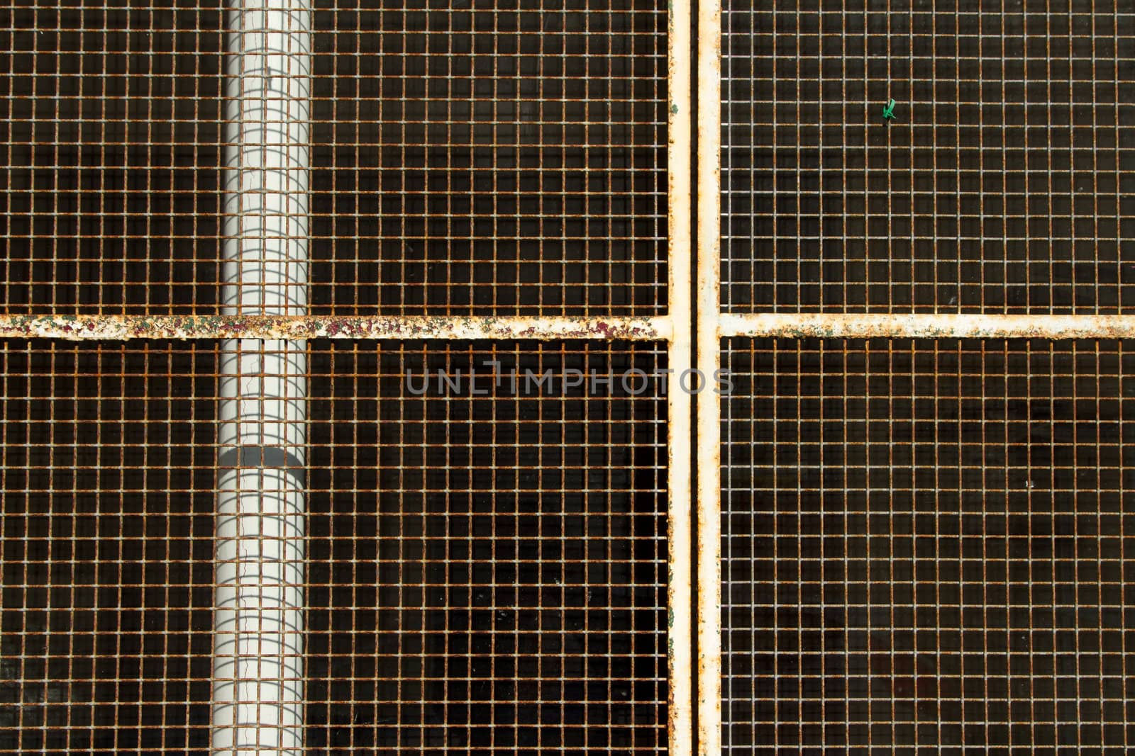 A white painted metal grill and frame with rust covers a dark area in the background.