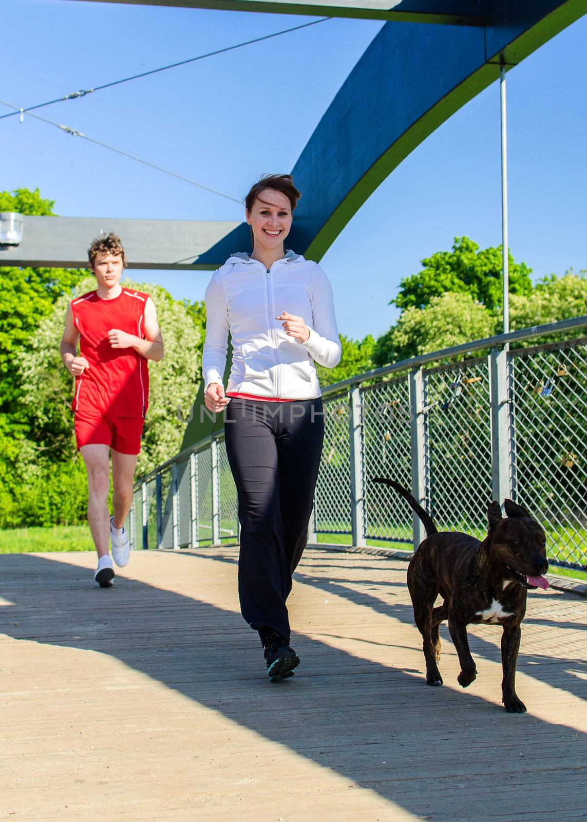 Couple running with dog across the bridge