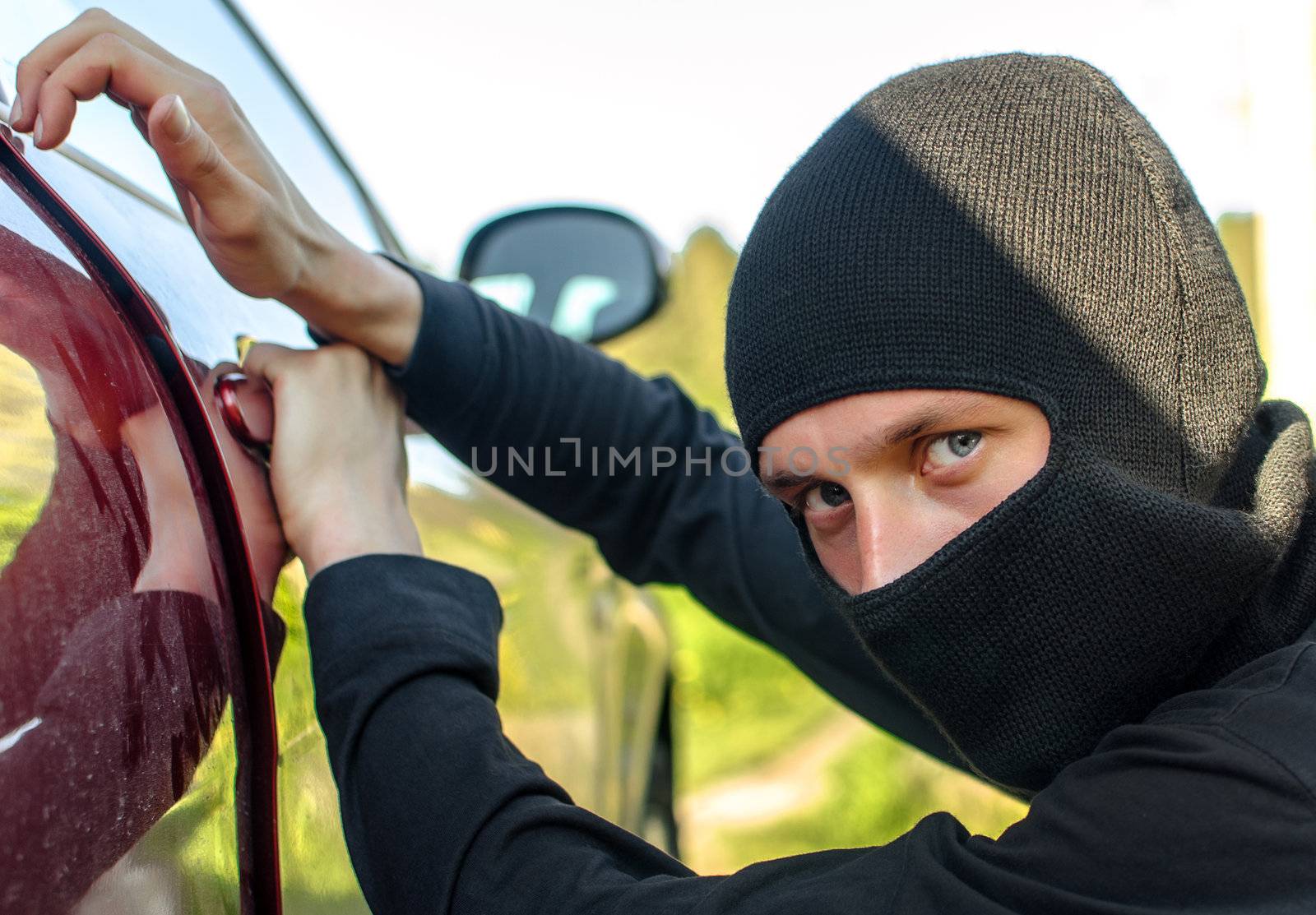 Thief in the mask breaks the door in the car