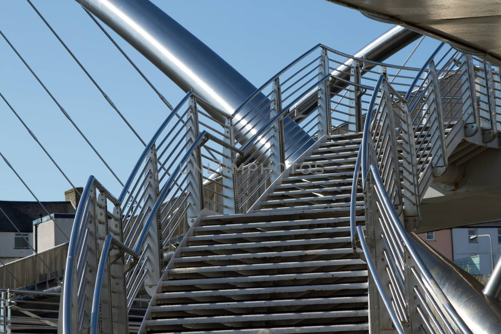 A set of stairs with safety railings leading to a bridge made of stainless steel against a blue sky.