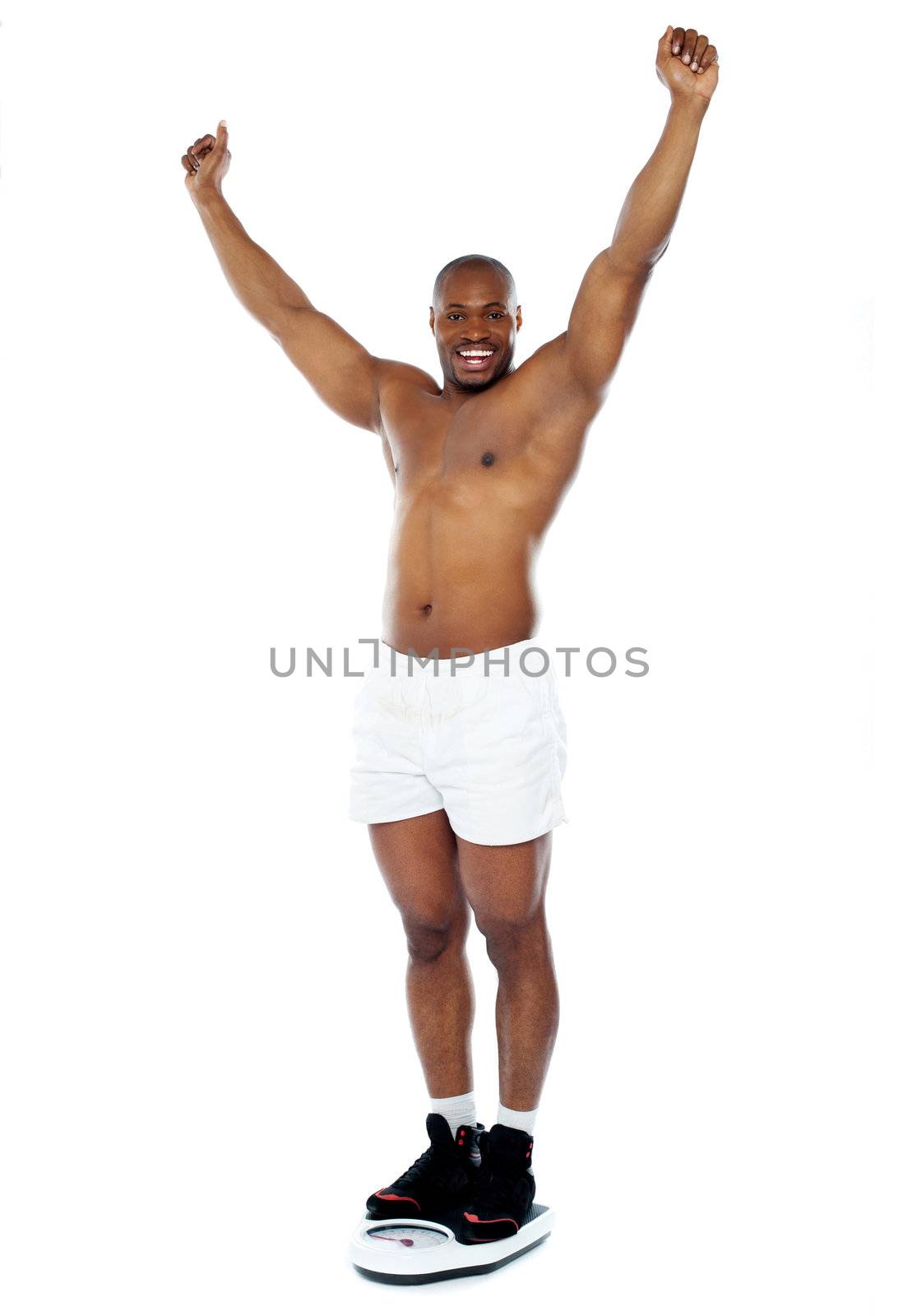 Smiling young man excited with arms up standing on weighing machine