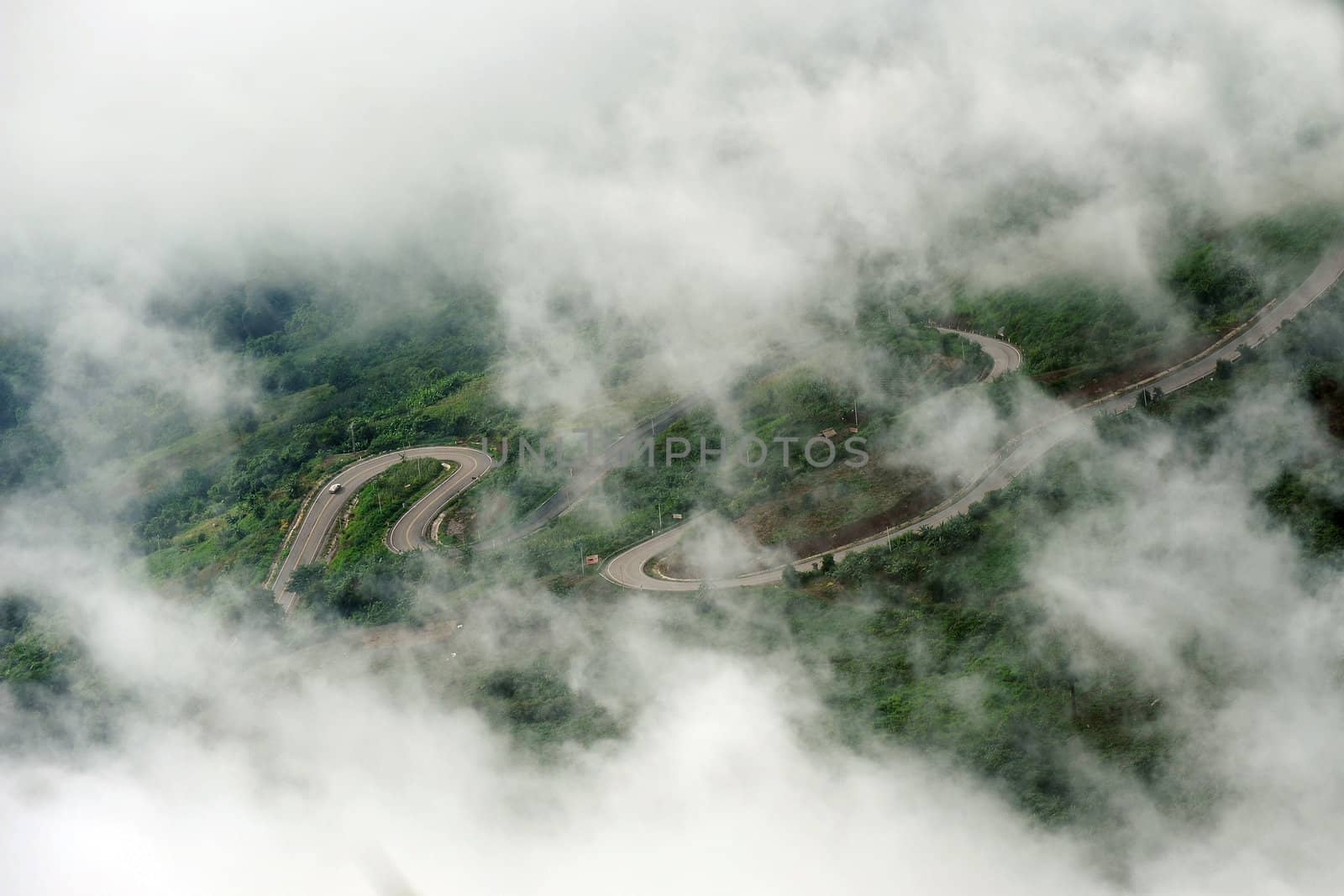 A road with a car driving in a mountain in clouds