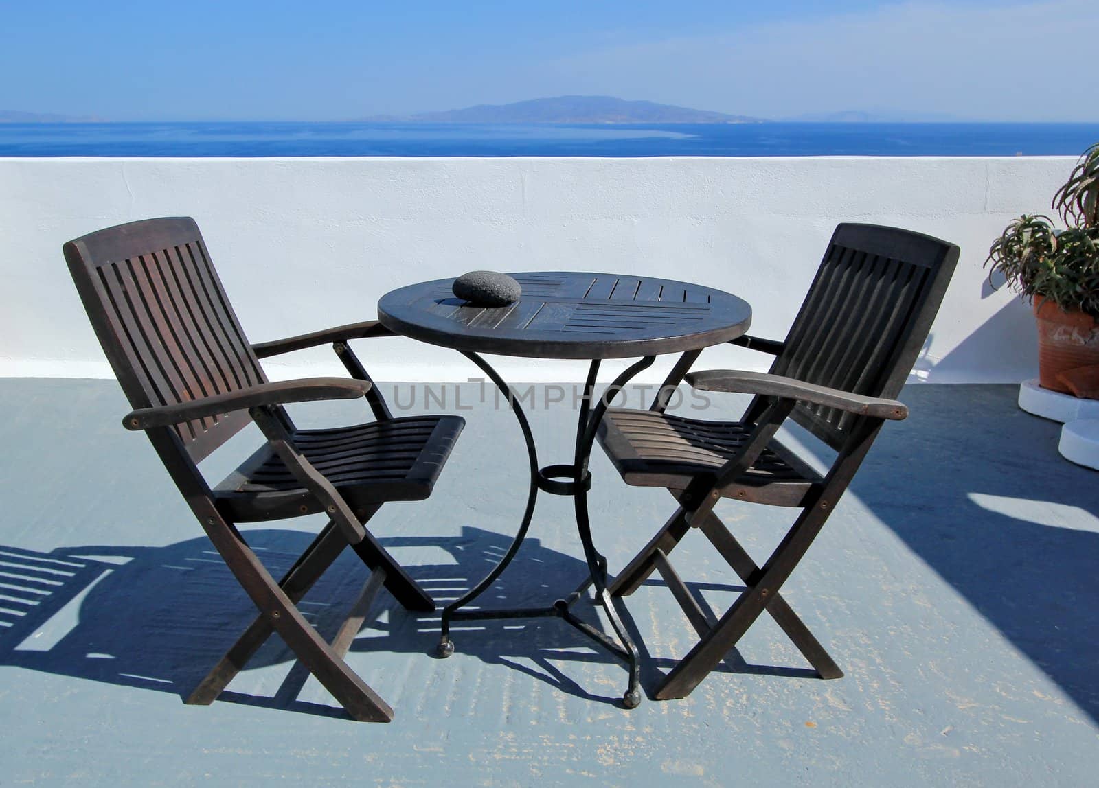 View on islands and Aegean sea from a balcony with tow black chairs and table made of wood at Oia, Santorini island, Greece
