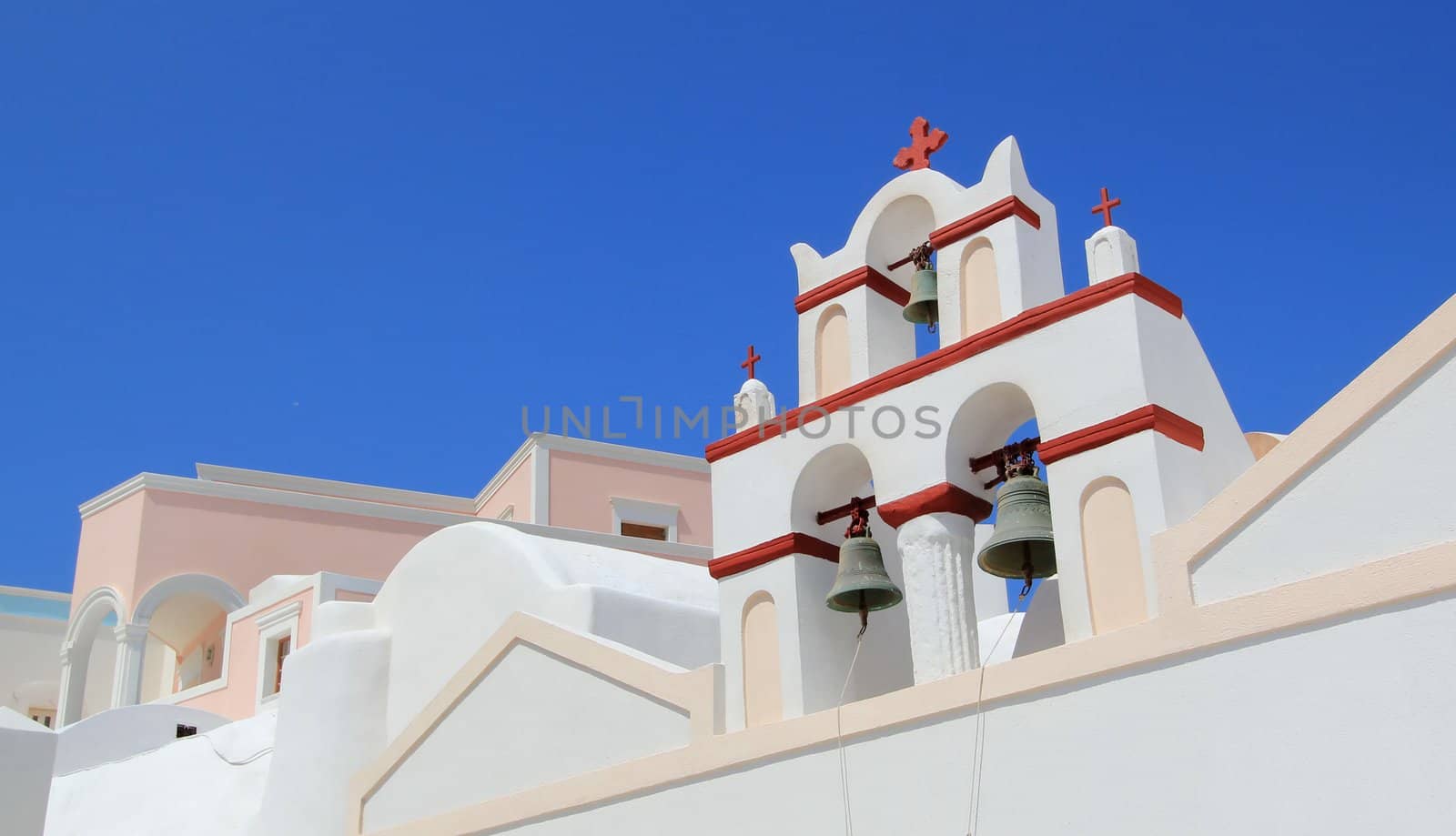 Close up of a white and red belfry of a typical greek church behind colorful houses by beautiful weather, Oia, Santorini, Greece