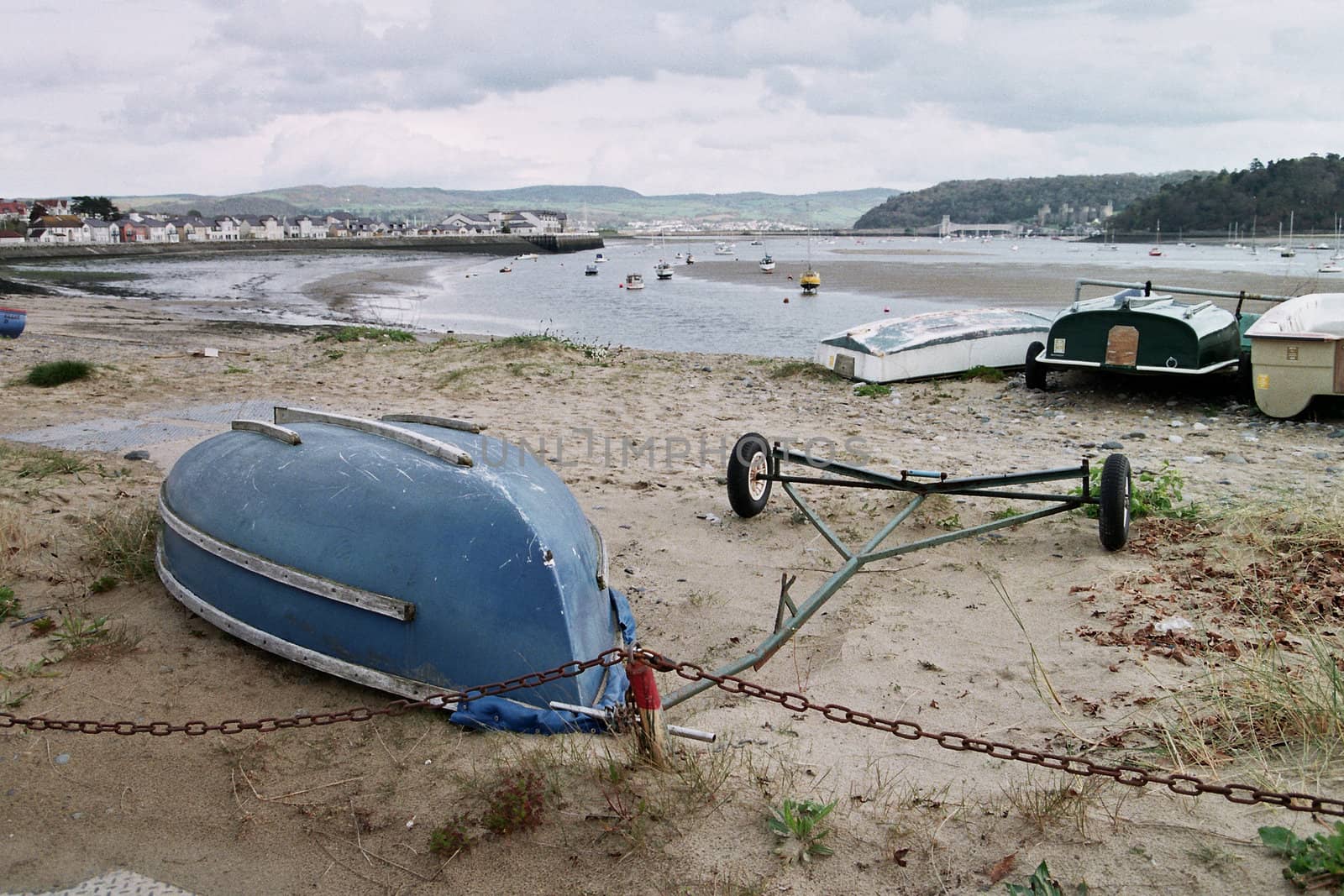 A collection of boat tenders on a beach with an estuary at low tide in the distance.