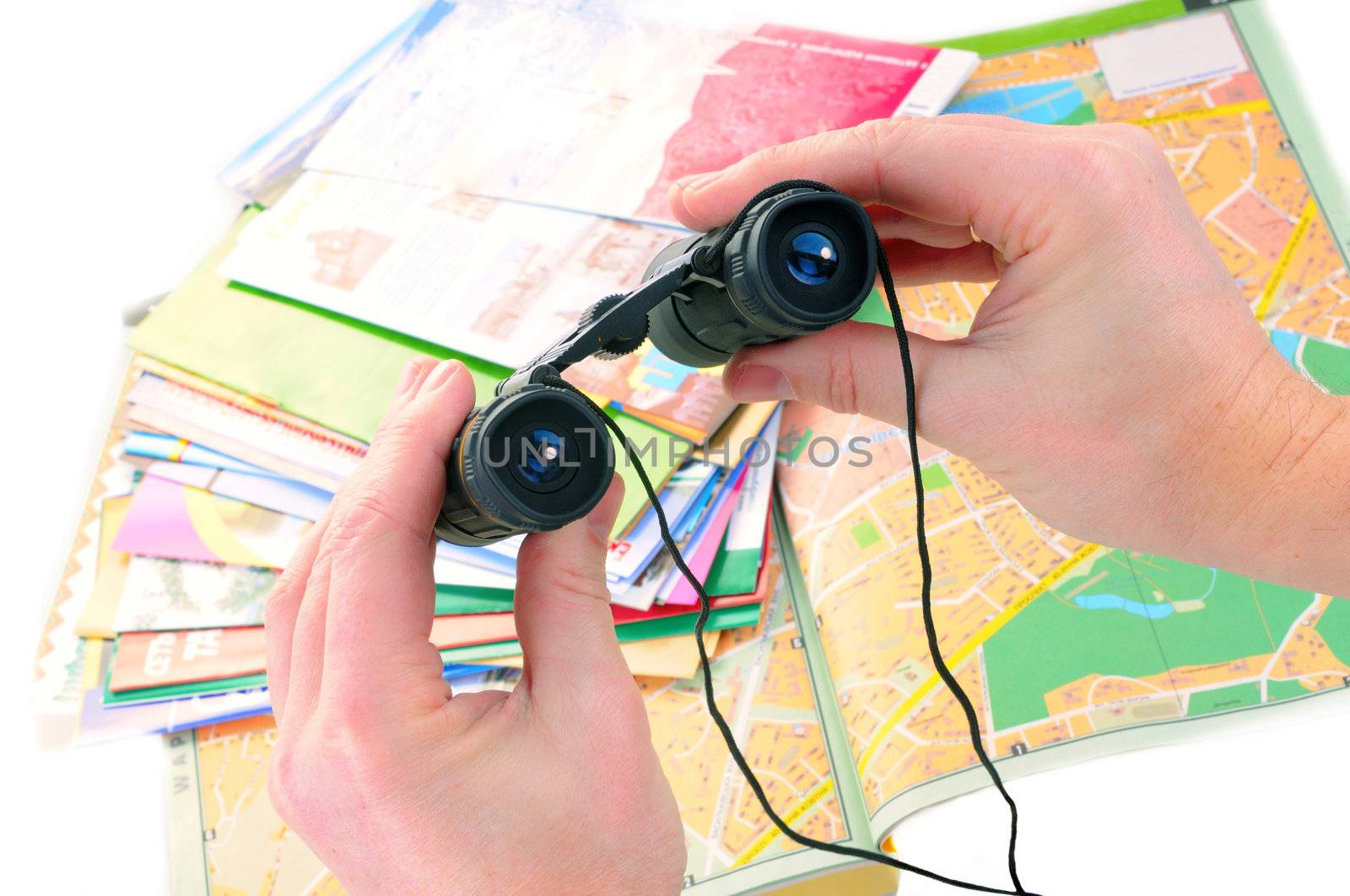 Black binoculars in male hands with maps on background