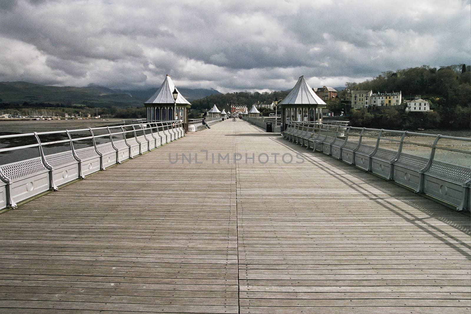 Bangor pier, Gwynedd, Wales, UK, with wooden boards and silver painted railings with cloudy mountains in the distance.