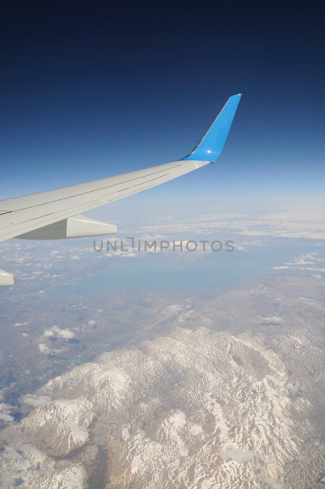 Airplane's wing under snow-covered mountains' peaks and lake