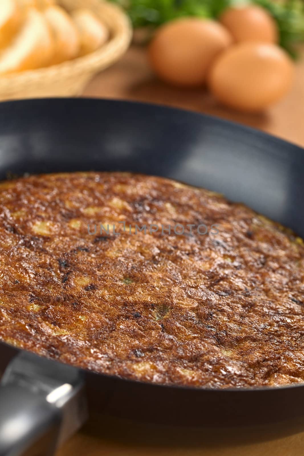 Preparing Spanish tortilla (omelette with potatoes) in frying pan with eggs and bread slices in the back (Selective Focus, Focus one third into the pan)