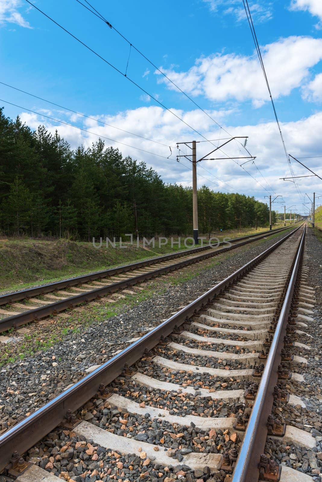 Railway with electric cables and blue sky. Focus on the front rail.