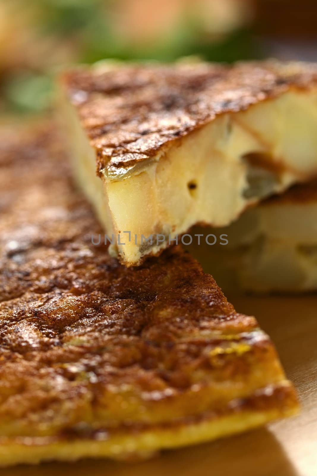 Fresh homemade Spanish tortilla (omelette with potatoes and onions) with a slice on top (Very Shallow Depth of Field, Focus on the tip of the tortilla slice on top)