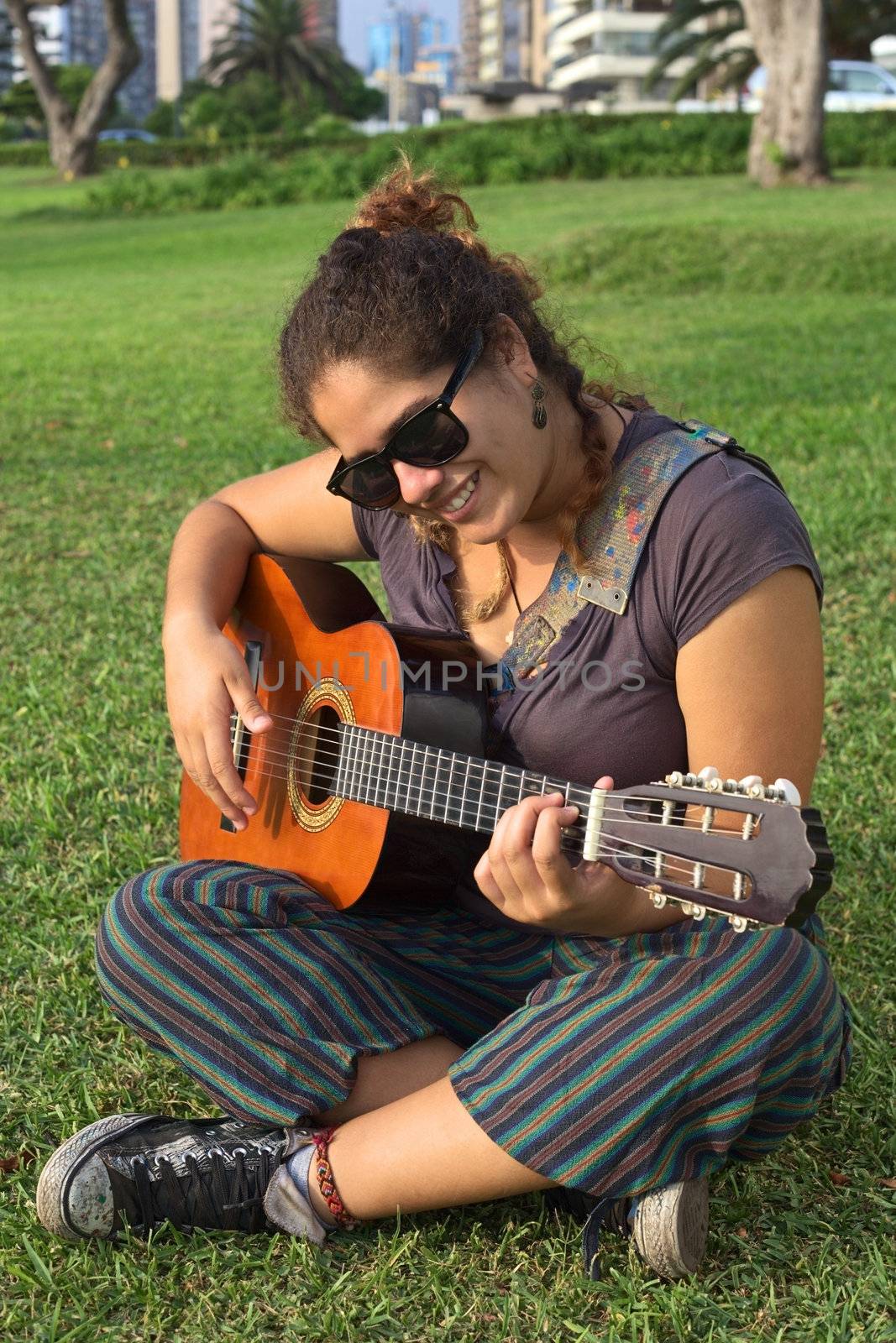 Beautiful smiling young Peruvian woman playing the guitar in a park (Selective Focus, Focus on the face of the woman)