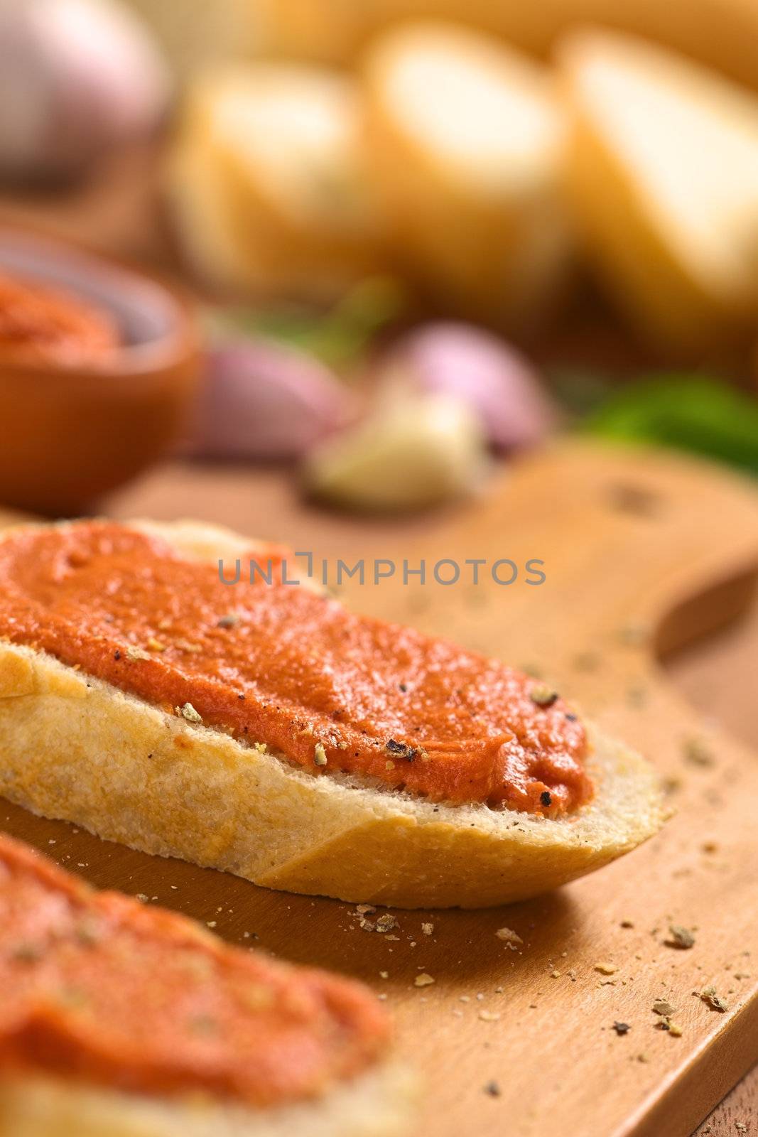 Homemade tomato-butter spread on baguette slices with fresh ground pepper on wooden board (Selective Focus, Focus on the front of the spread)