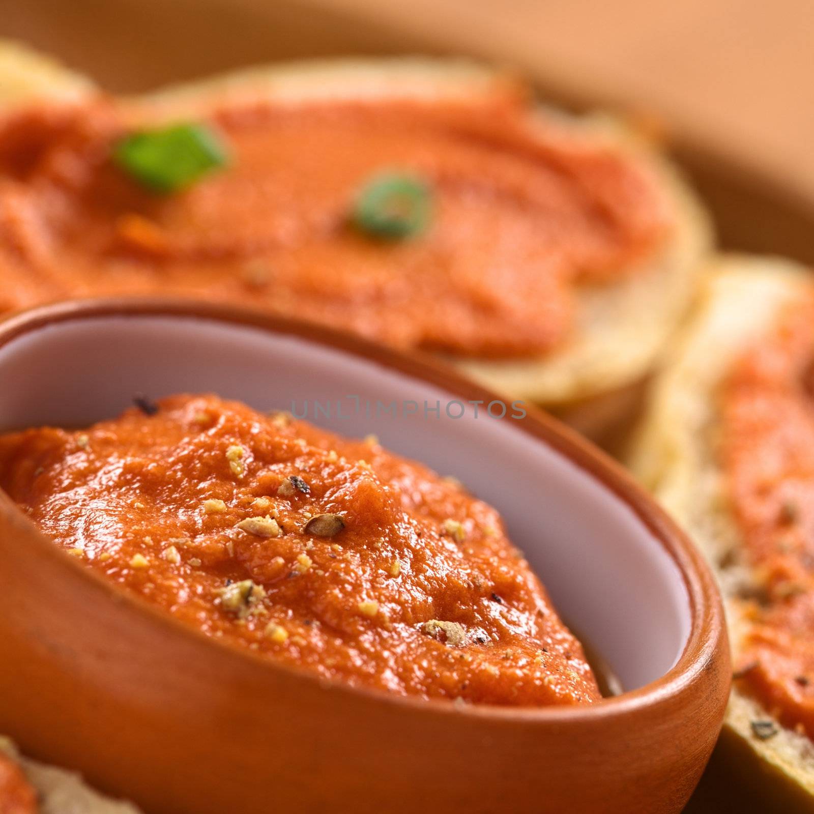Fresh homemade tomato-butter spread in small bowl with fresh ground pepper on top surrounded by canapes (Selective Focus, Focus on the middle of the spread in the bowl)