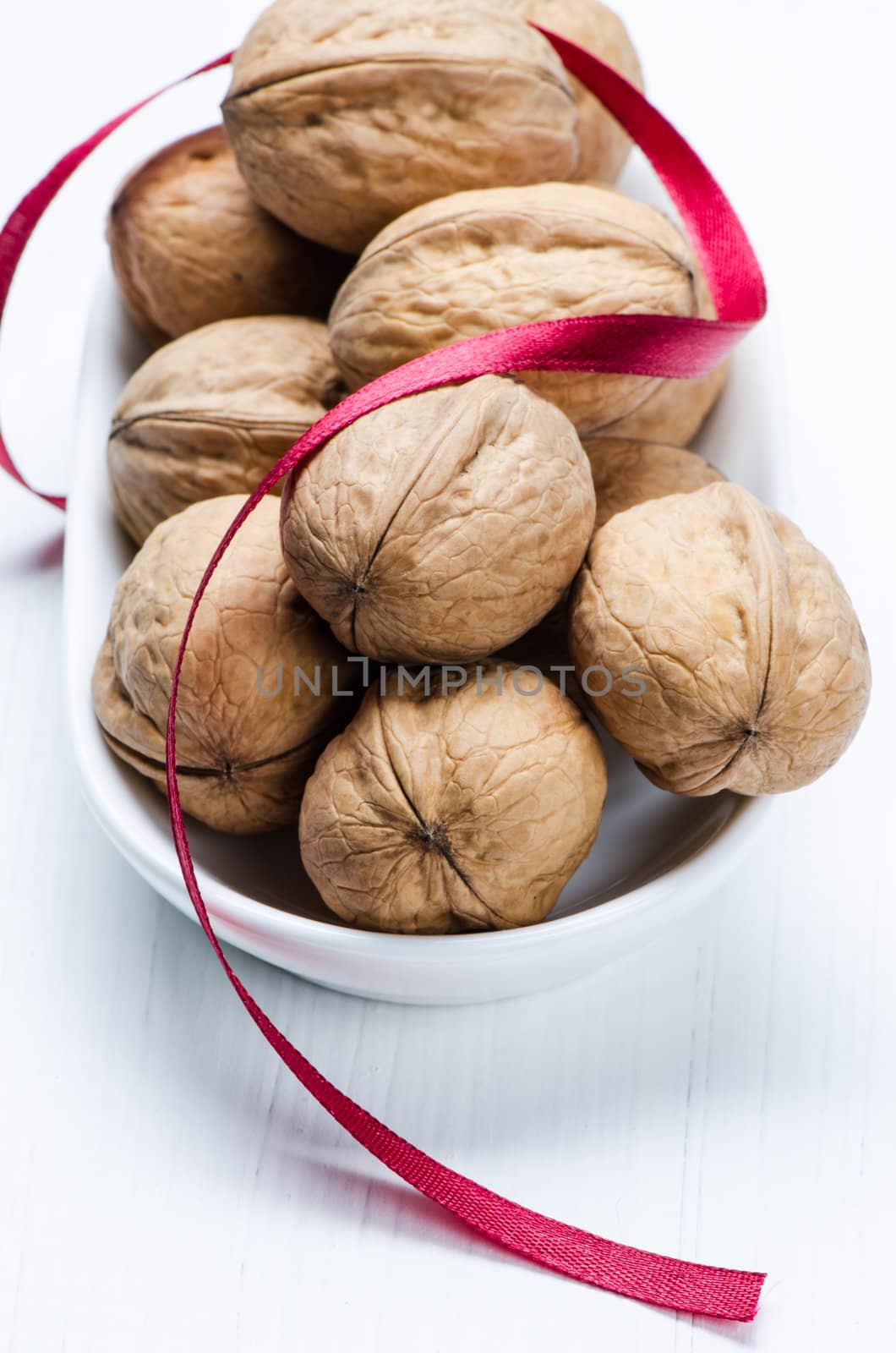 Bunch walnuts in white plate on wooden white table with red ribbon.