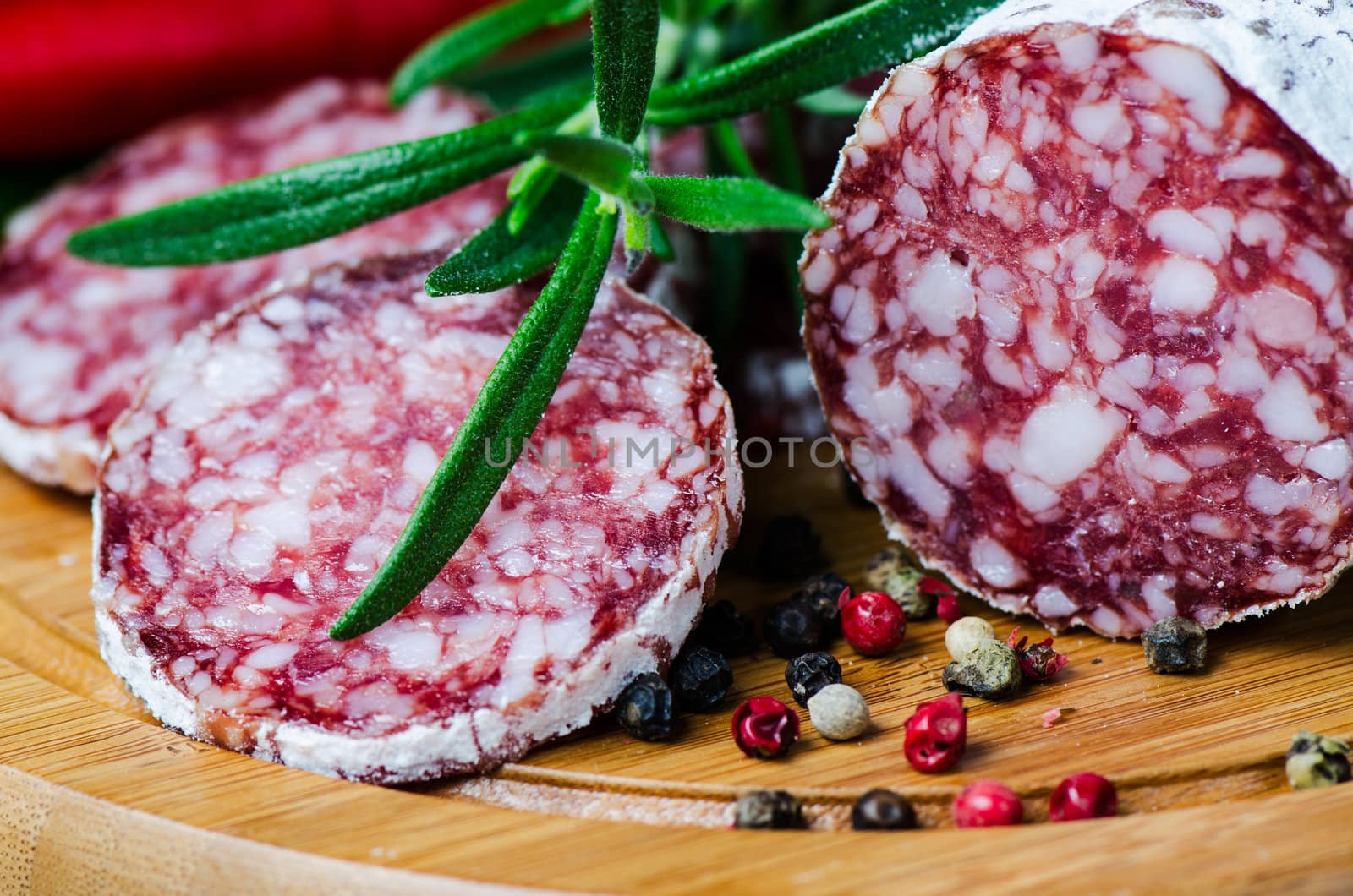 Close up salami peper corns rosemary on cutting board by Nanisimova