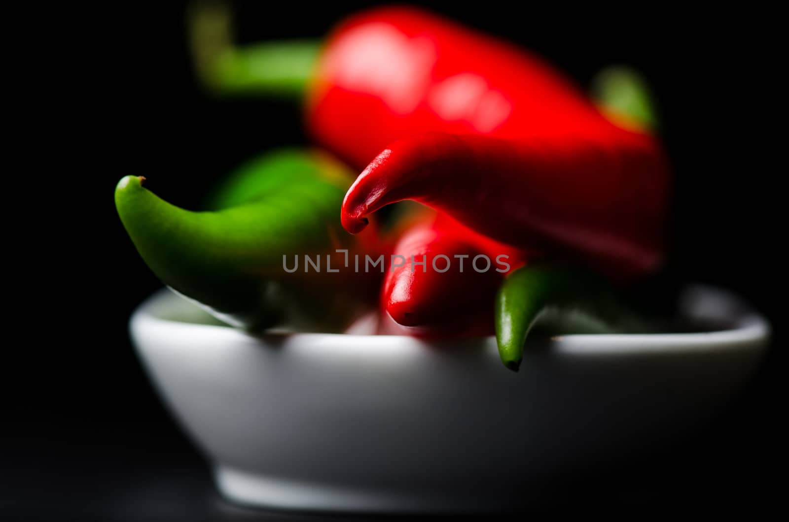Green and red chili peppers on black  background by Nanisimova