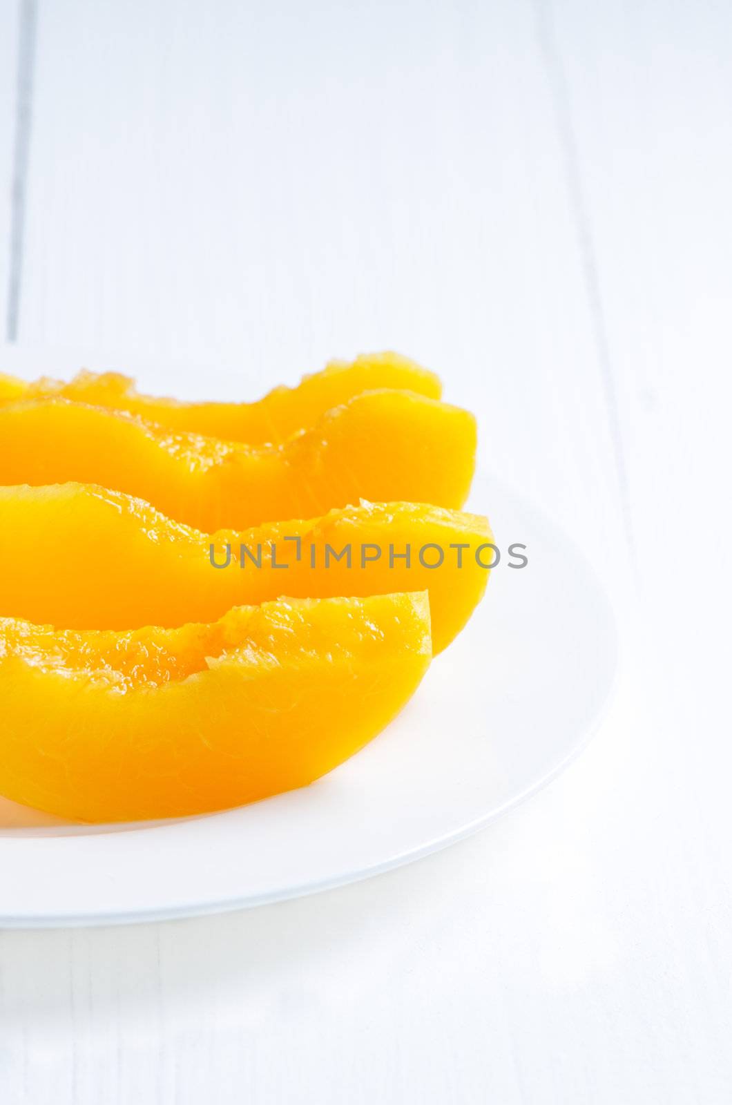 Slices canned peach on white wooden table