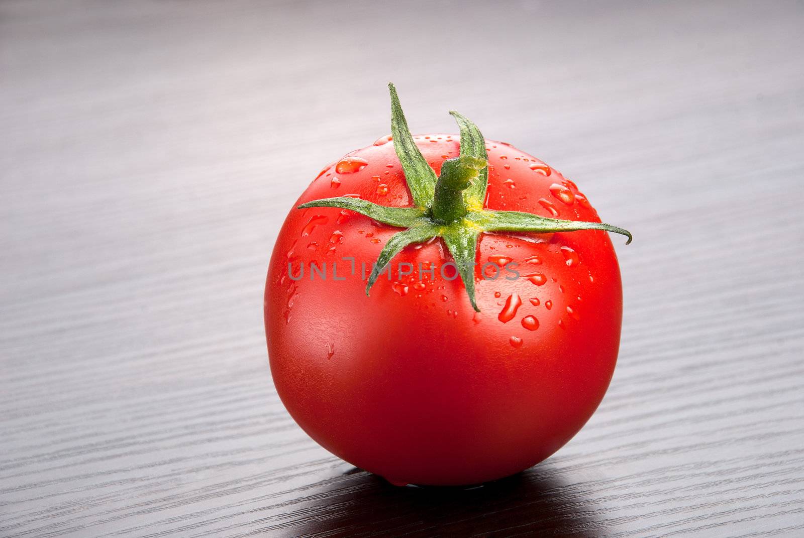 one fresh tomato with drops of water on the wooden background