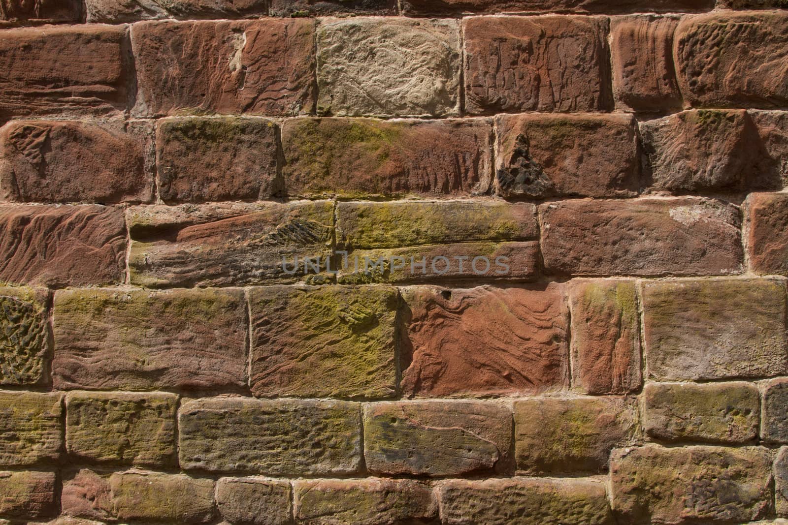 A wall constructed of red, cut sandstone with curves and textures held together with cement pointing.