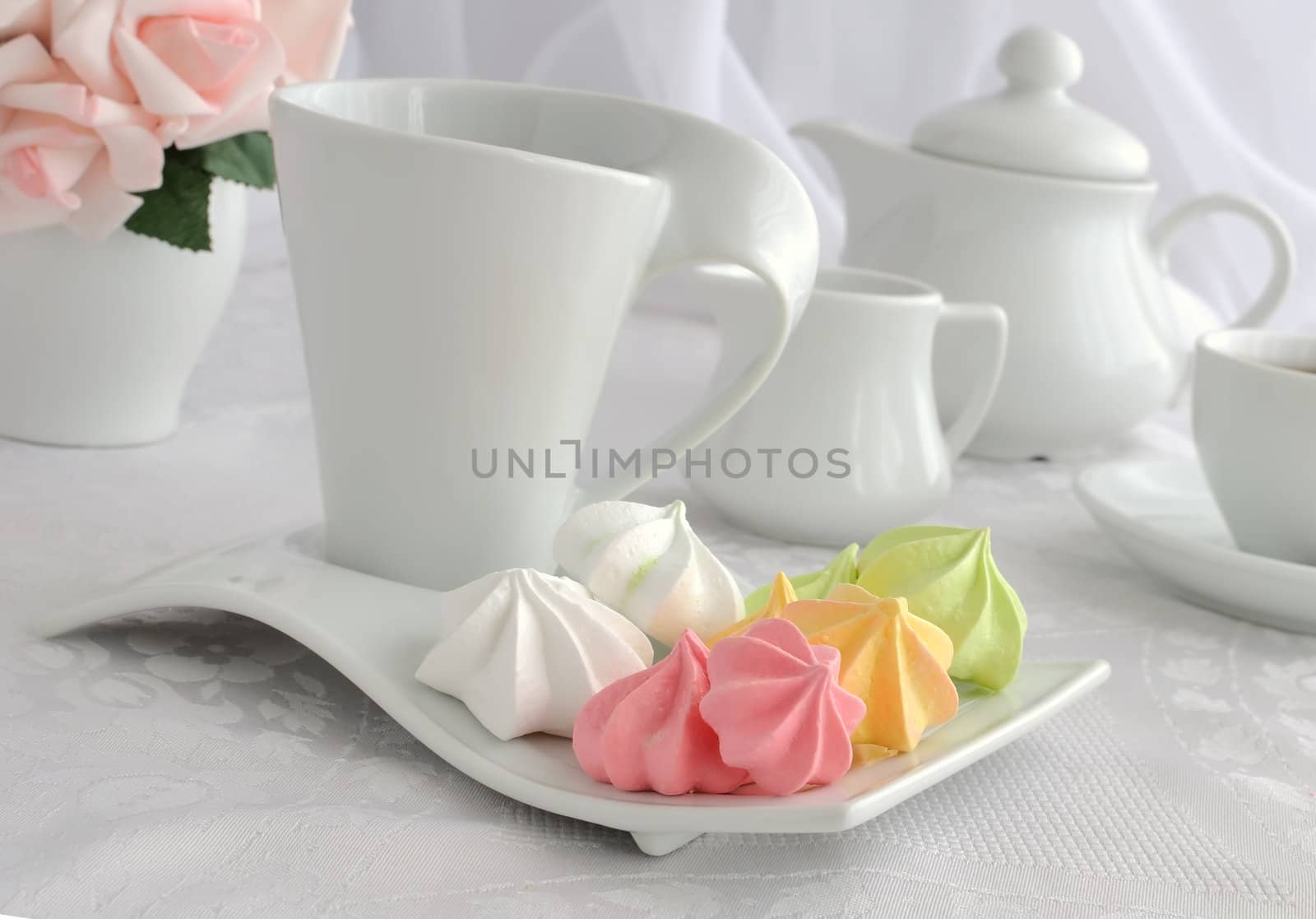 Meringue cookies of different colors on a plate with a cup of co by Apolonia