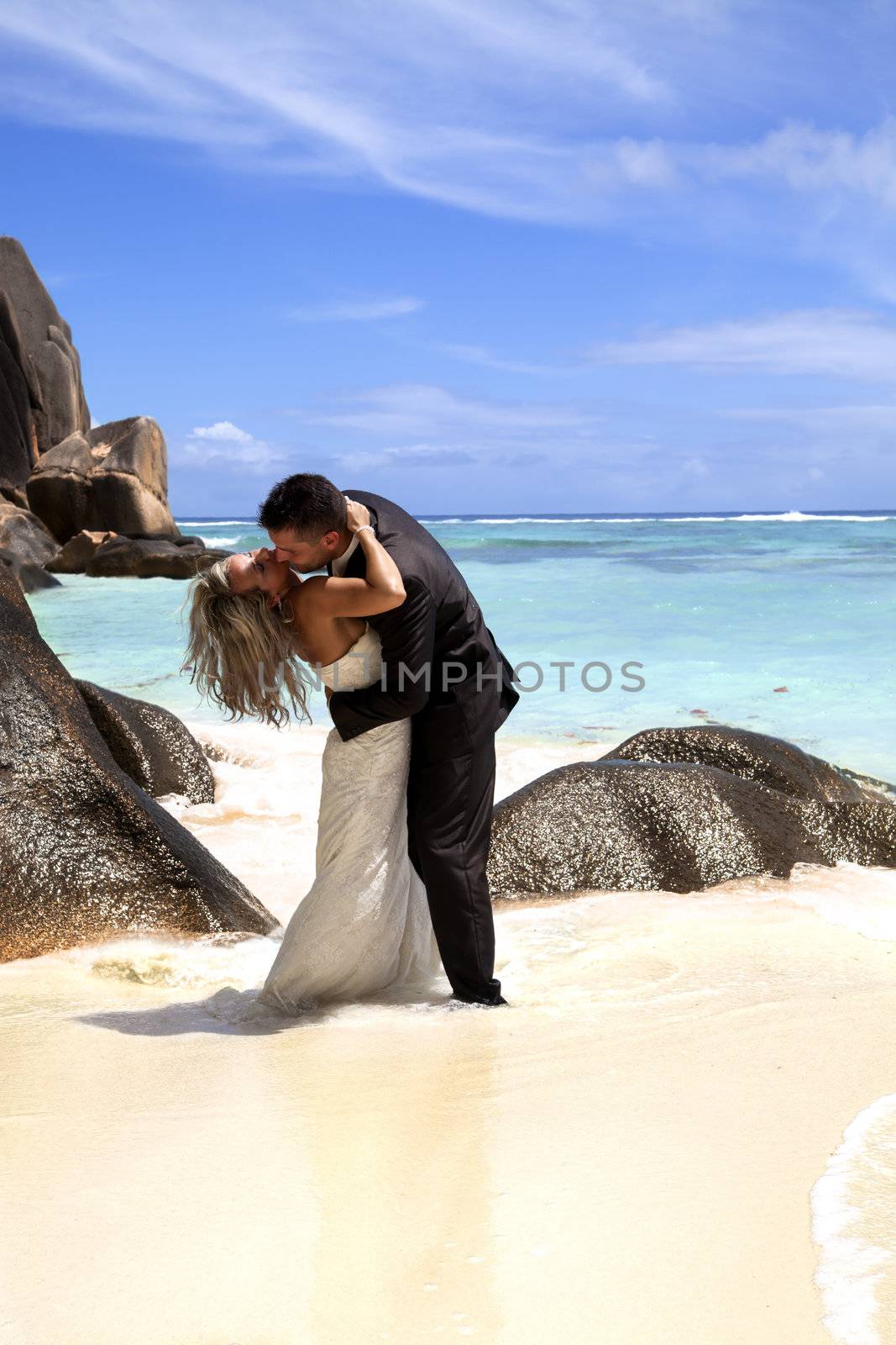 Romantic bridal couple enjoying a passionate kiss on a tropical beach with ocean backdrop