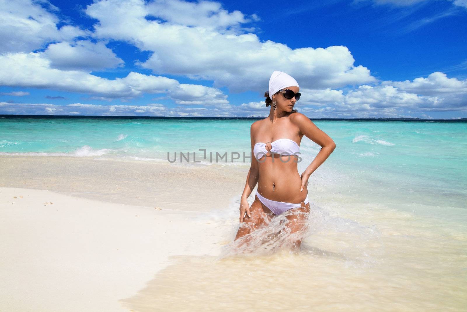 Sexy shapely woman wearing a bandanna and bikini standing in ocean surf on a tropical beach with copyspace