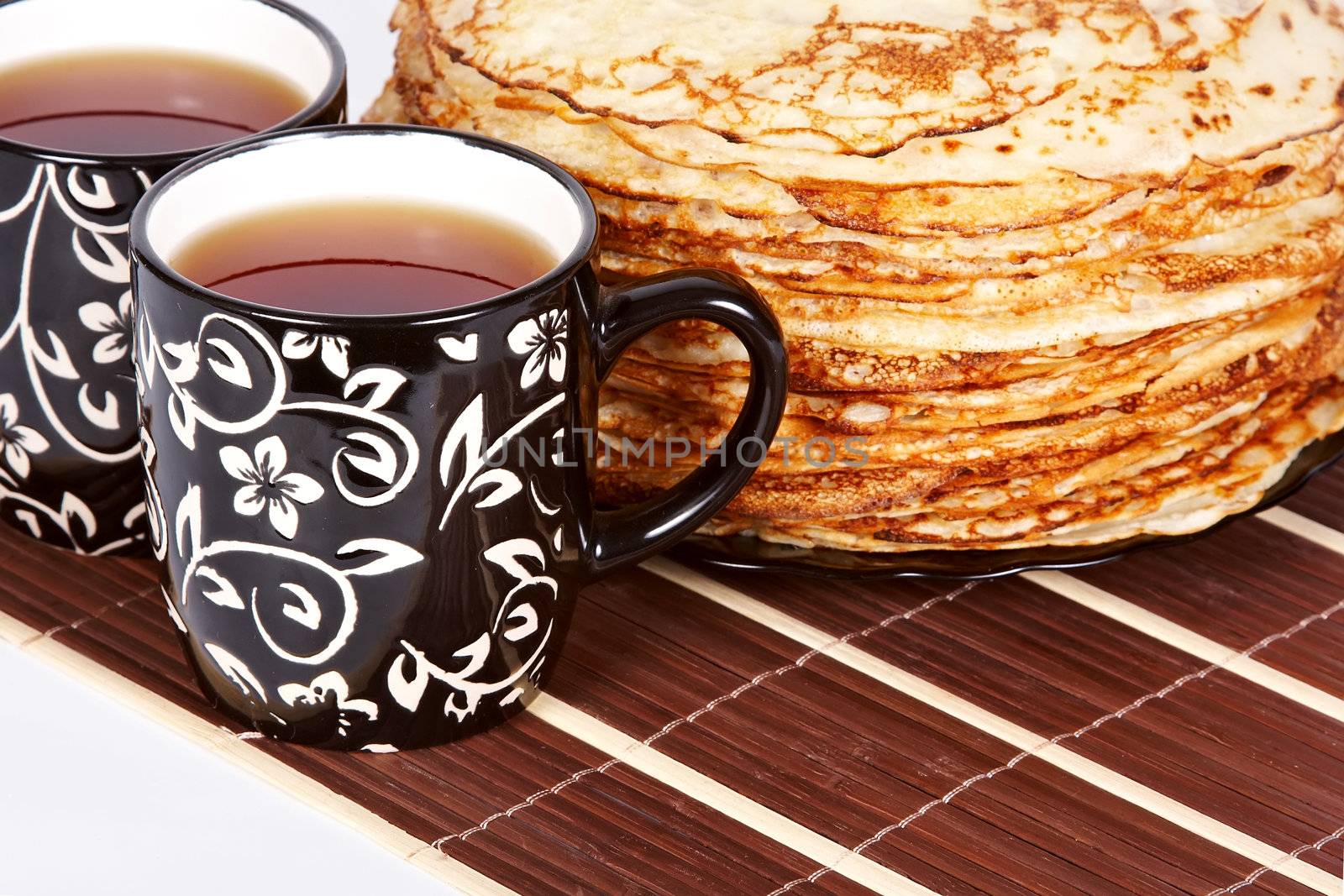 Cups with tea and a pile of pancakes on a plate