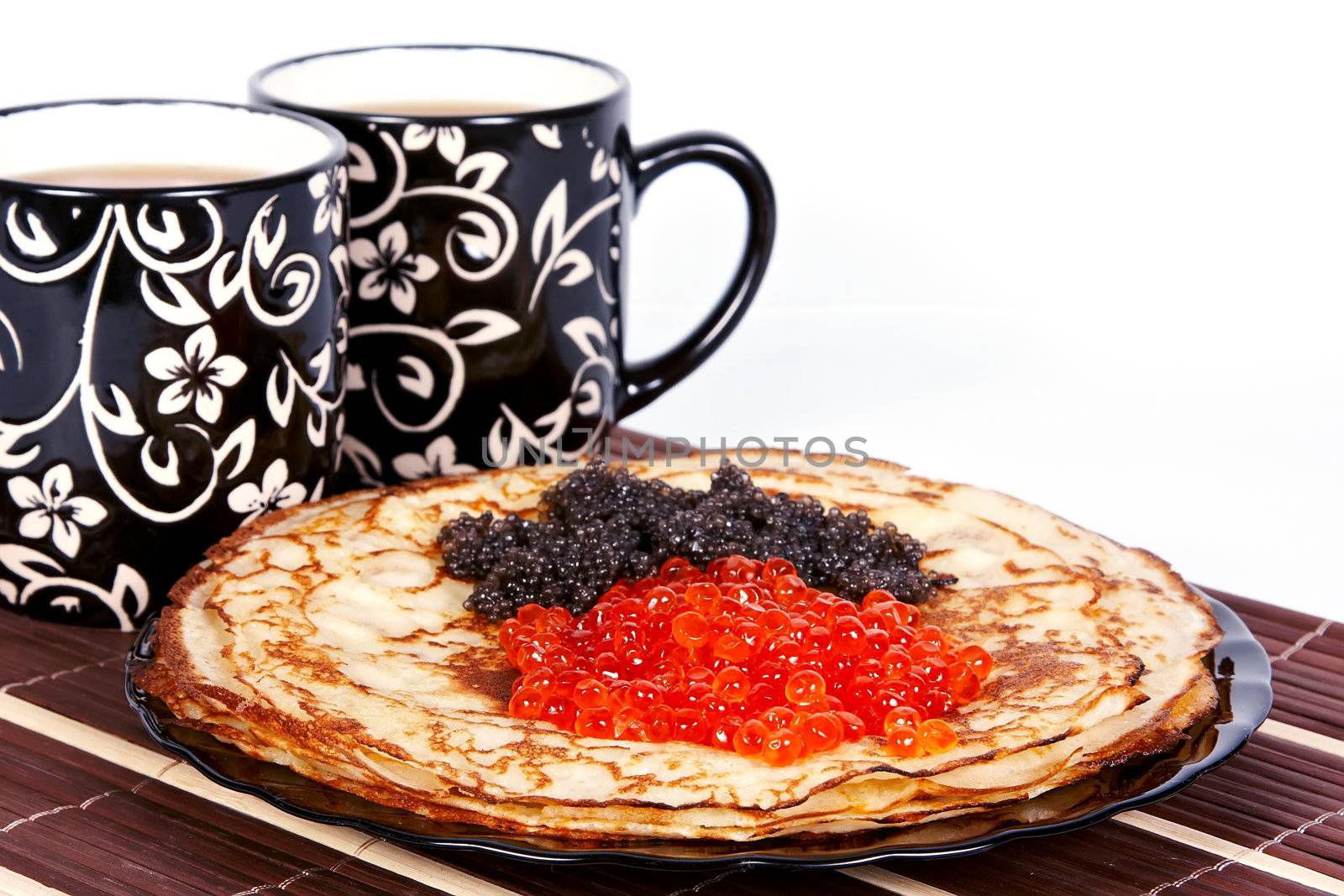 Cups with tea and a pile of pancakes with caviar on a plate