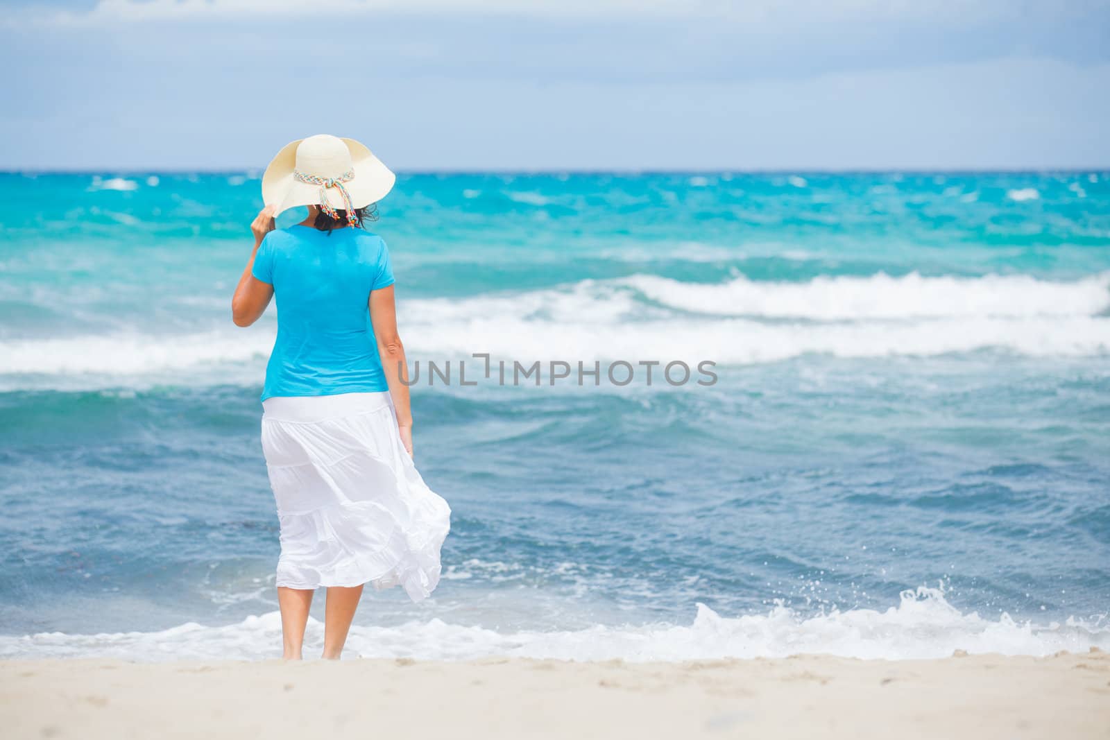 Happy beautiful woman in the beach hat looking at the sea