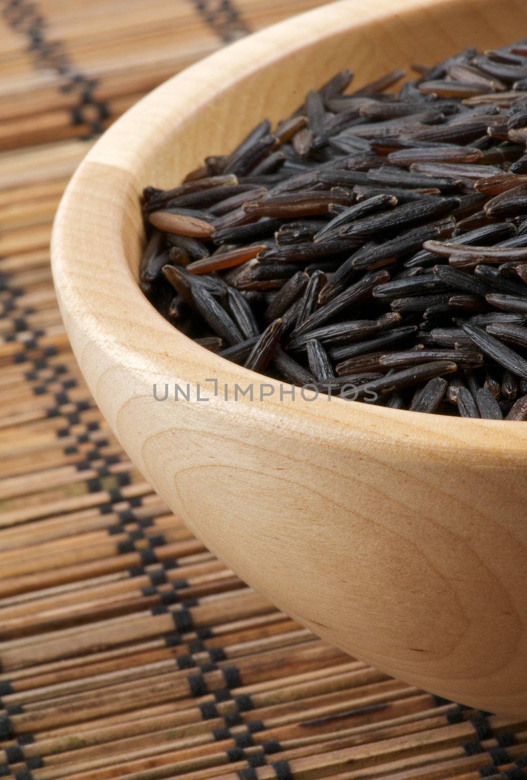 Wild brown rice in wooden bowl isolated on strawmat background