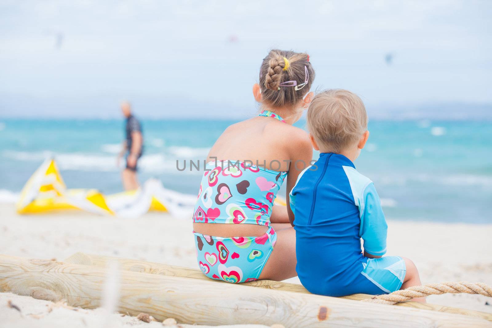 Back view cute 2 years old boy with his sister looking at kiting on tropical beach