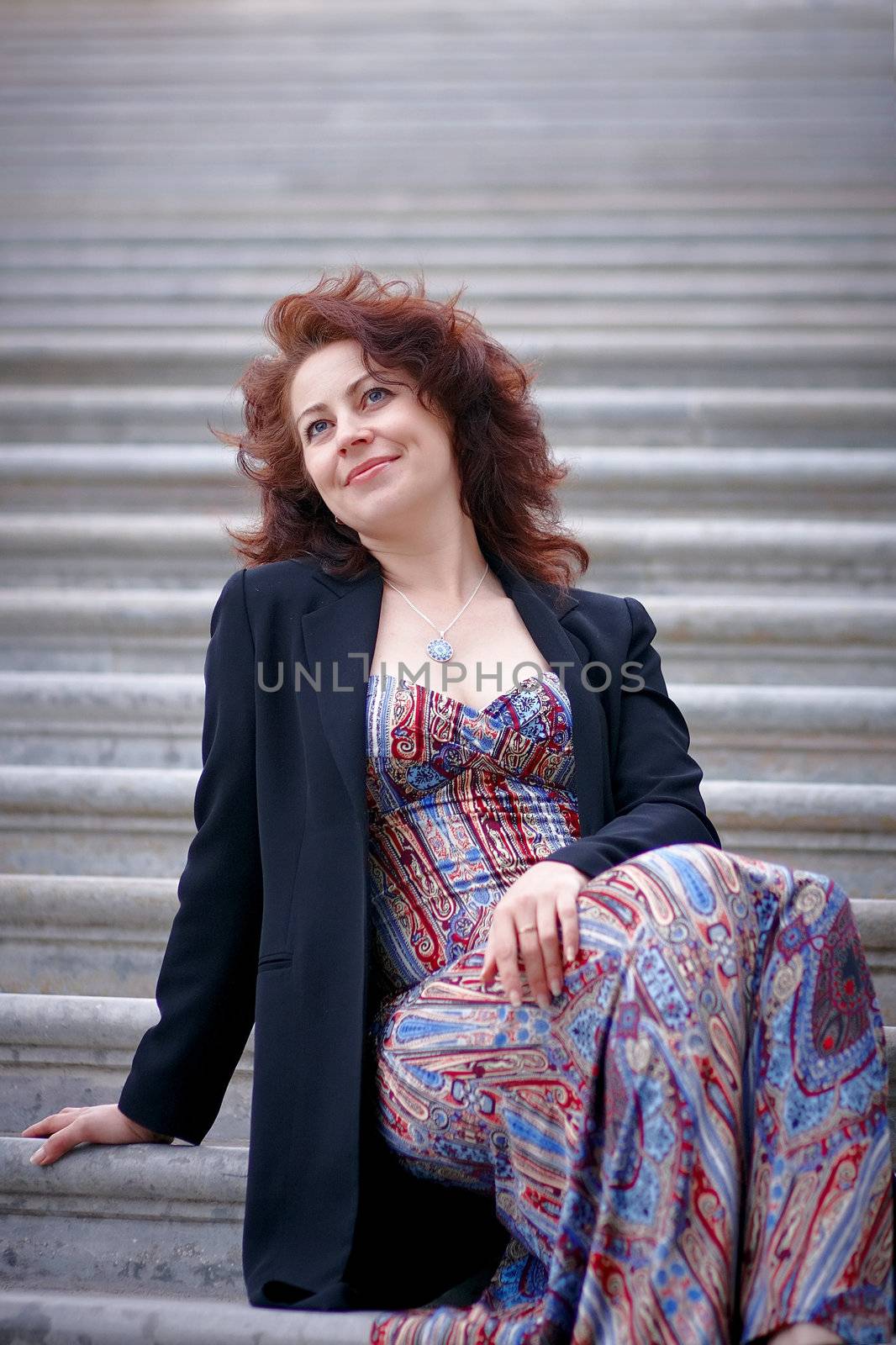 Portrait of the beautiful dreaming woman in a jacket sitting on steps