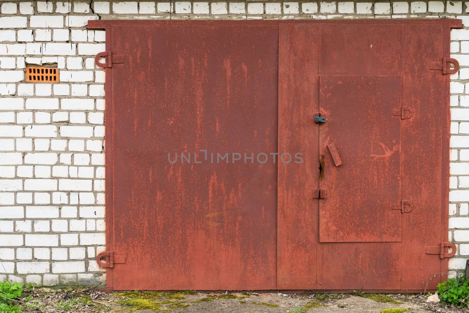 Aged closed red metal garage gate on white brick wall