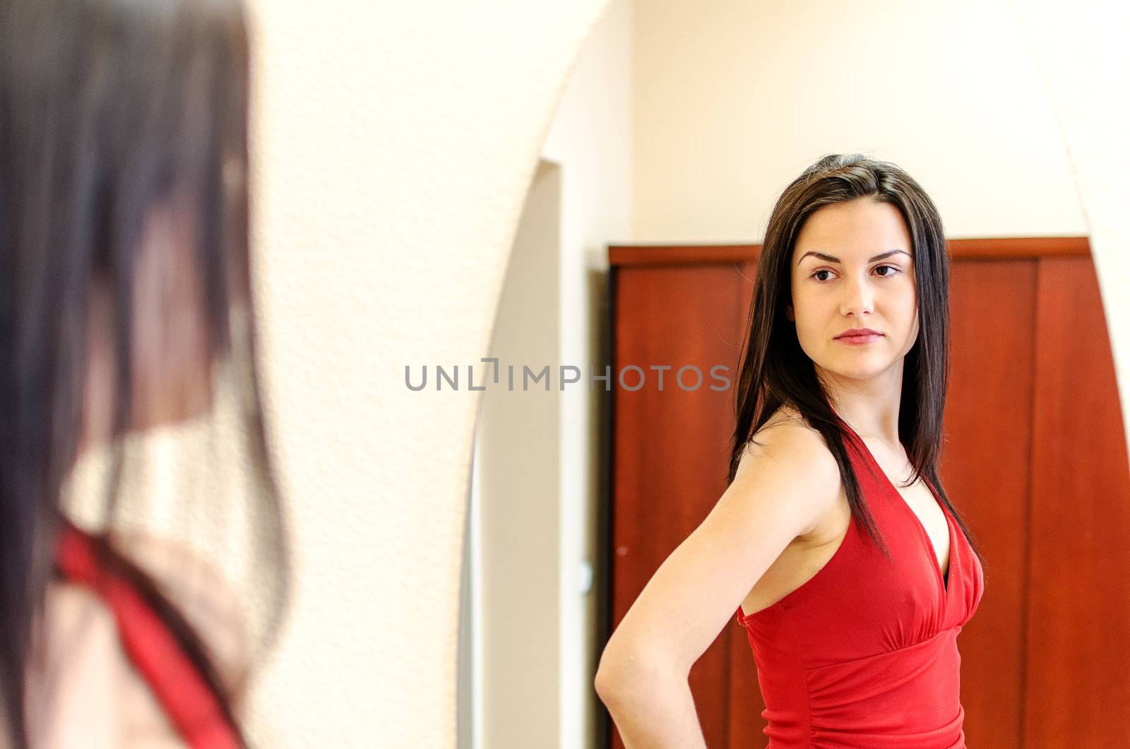 Beautiful girl in red dress posing in front of a mirror