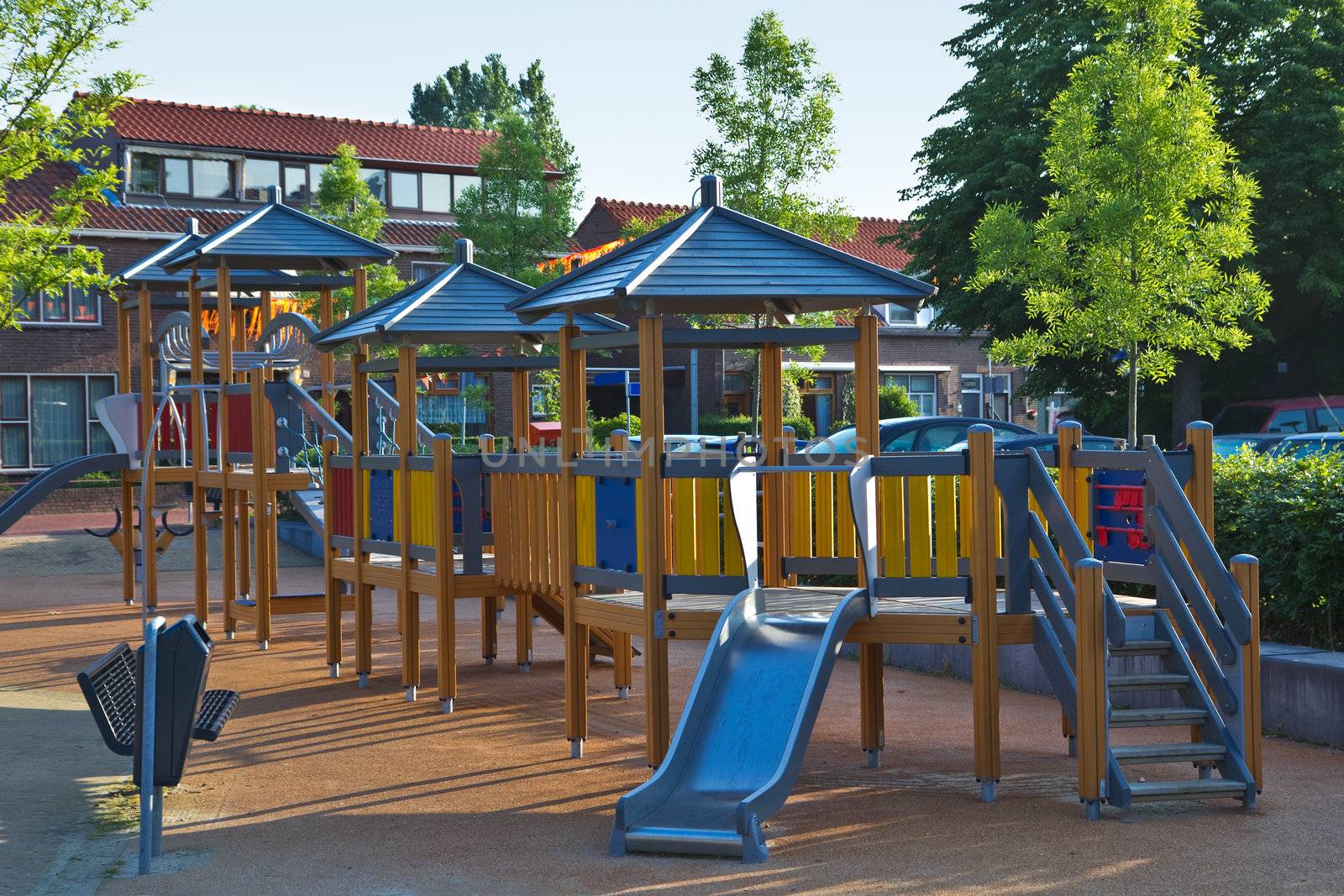 Public playground with colorful wooden climbing construction, swing, slides and rubber floor for safe playing