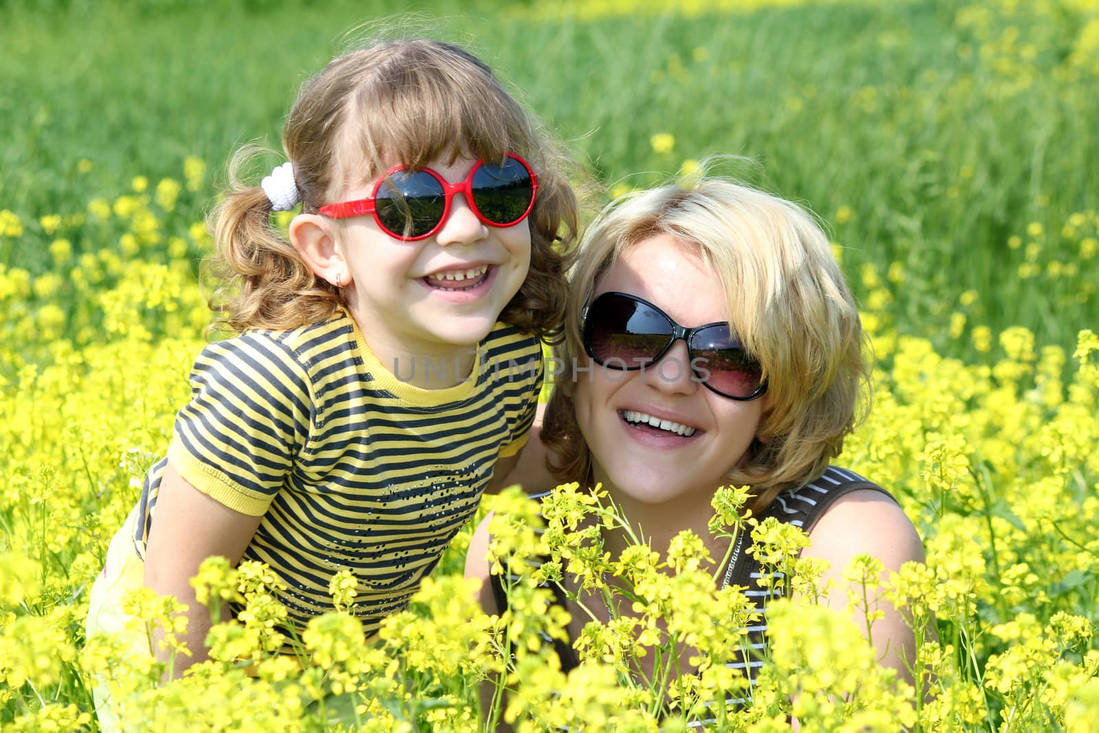 happy mother and daughter in yellow flowers field by goce