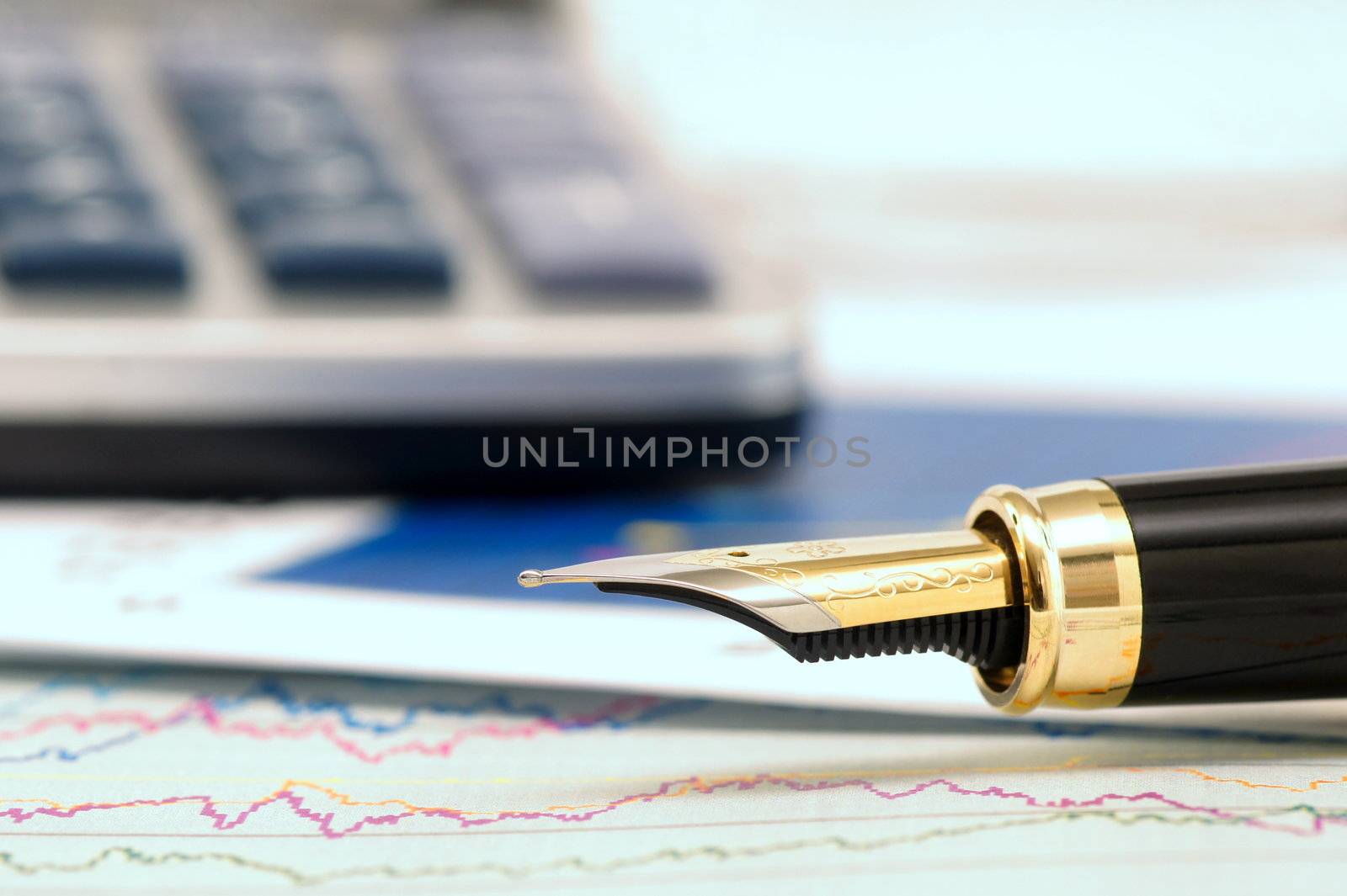 A nib of a Fountain pen over a graph and a calculator background with shallow depth of field.