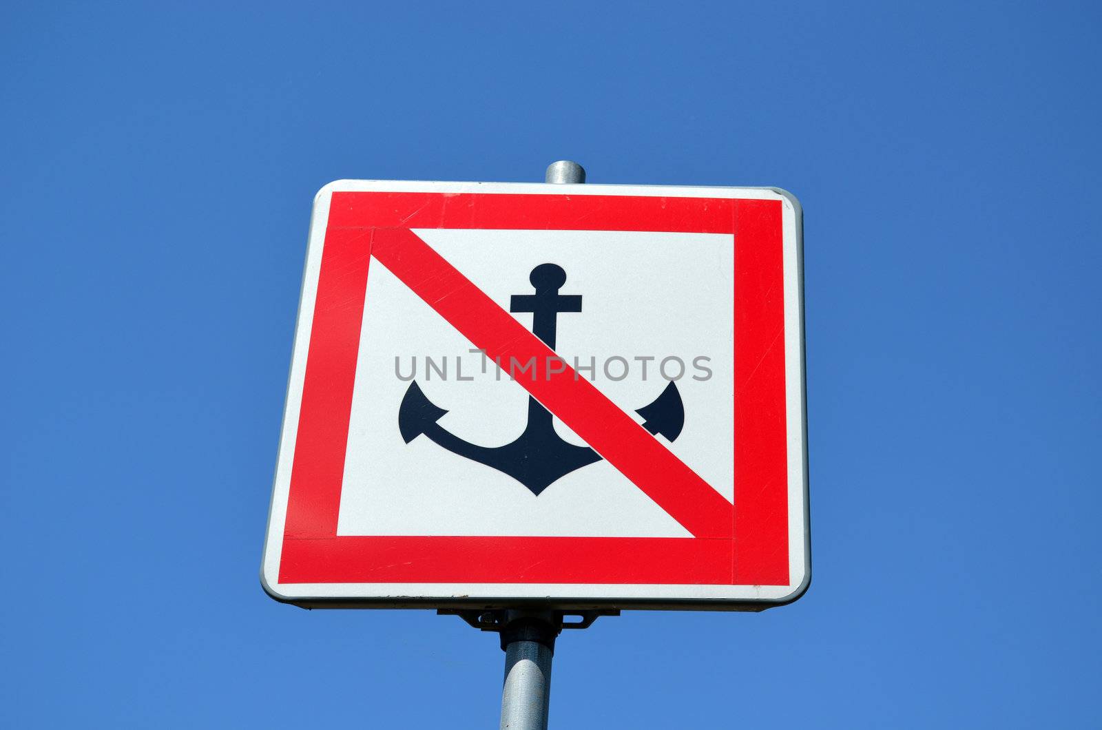 Warning sign prohibiting ships mooring riverside on background of blue sky. Anchor crossed red line.