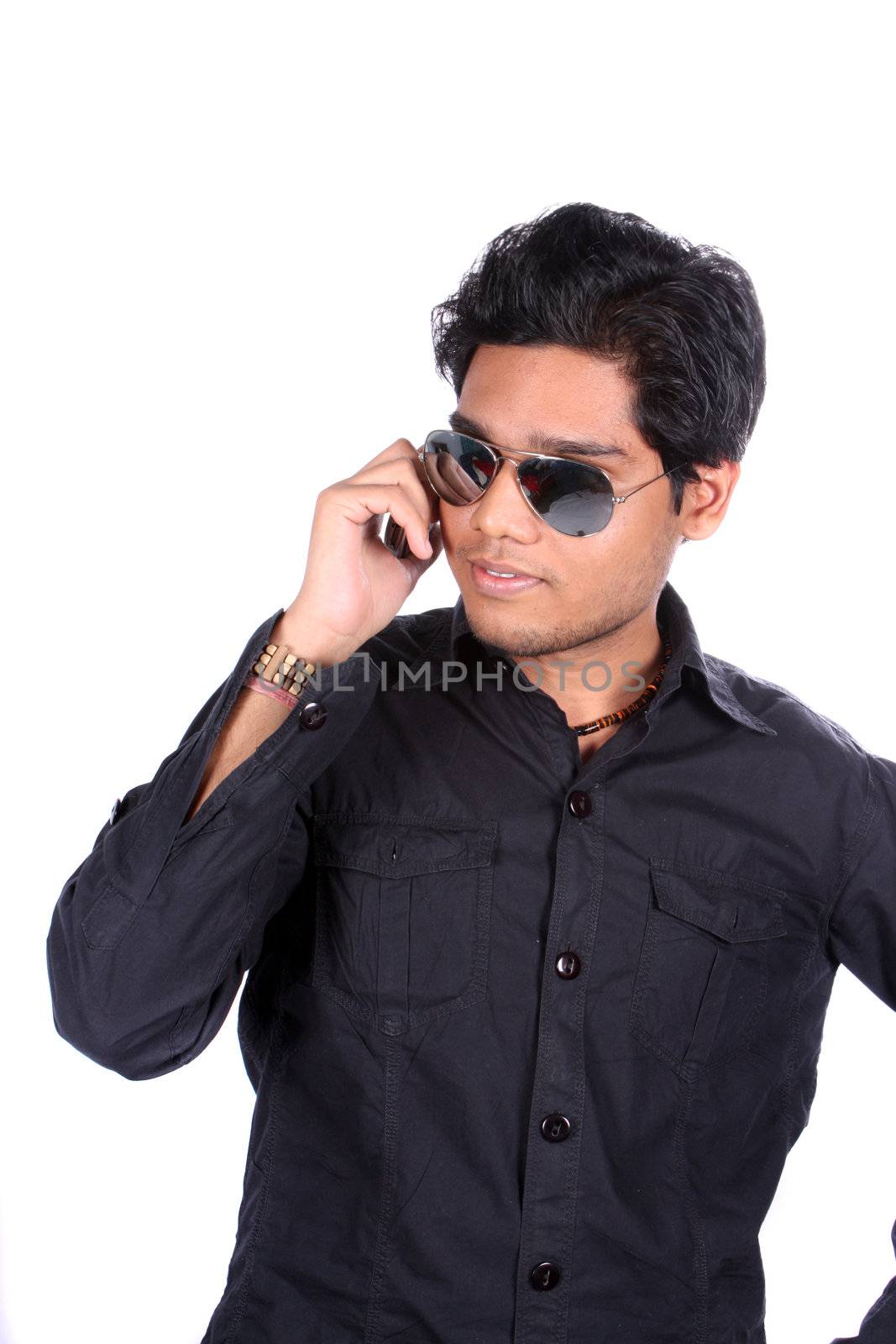 A young Indian guy wearing sunglasses stylishly talking on the phone, on white studio background.